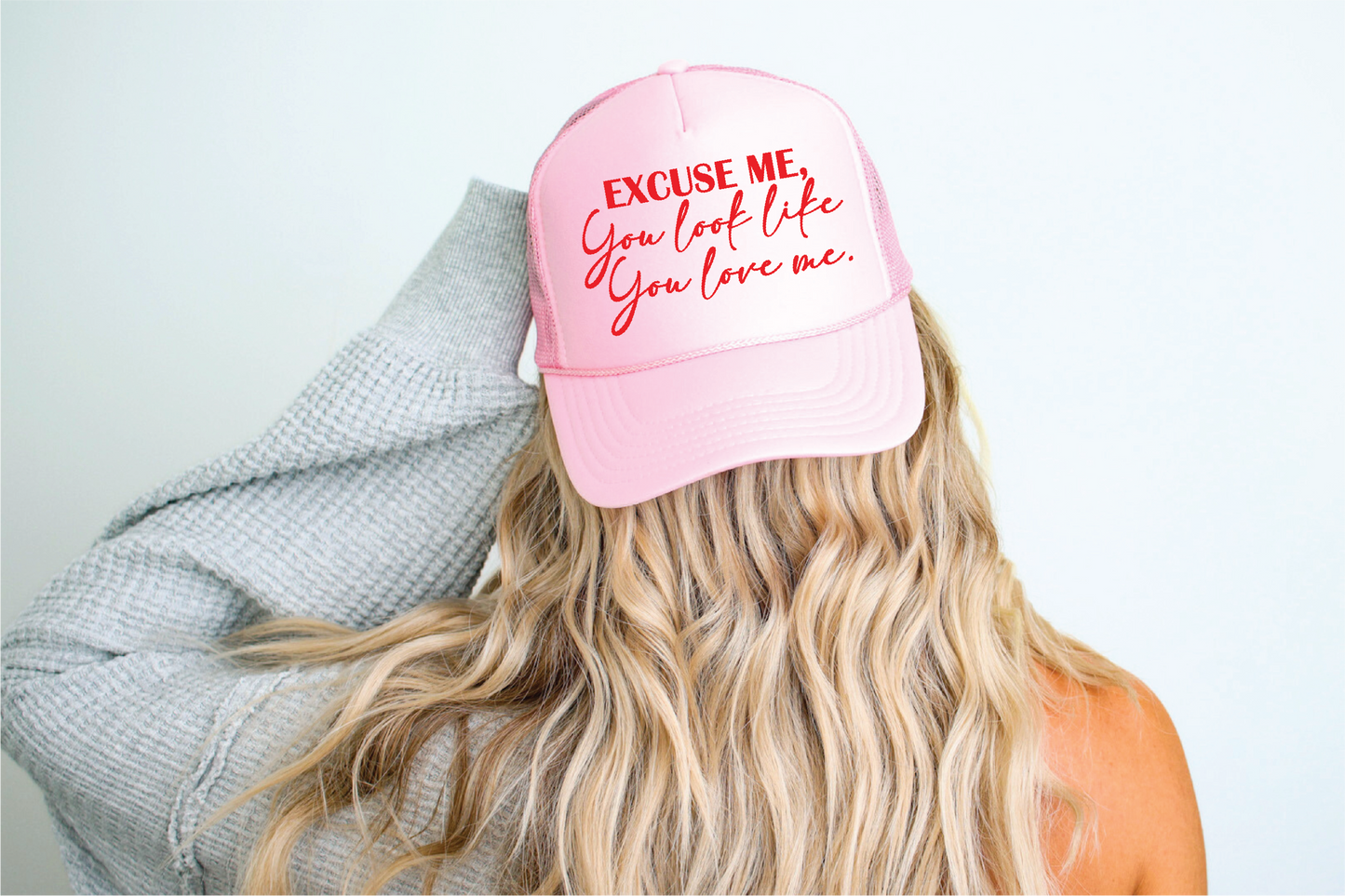 A person wearing a pink foam trucker hat with the text 'EXCUSE ME, You look like you love me.' printed on the front.