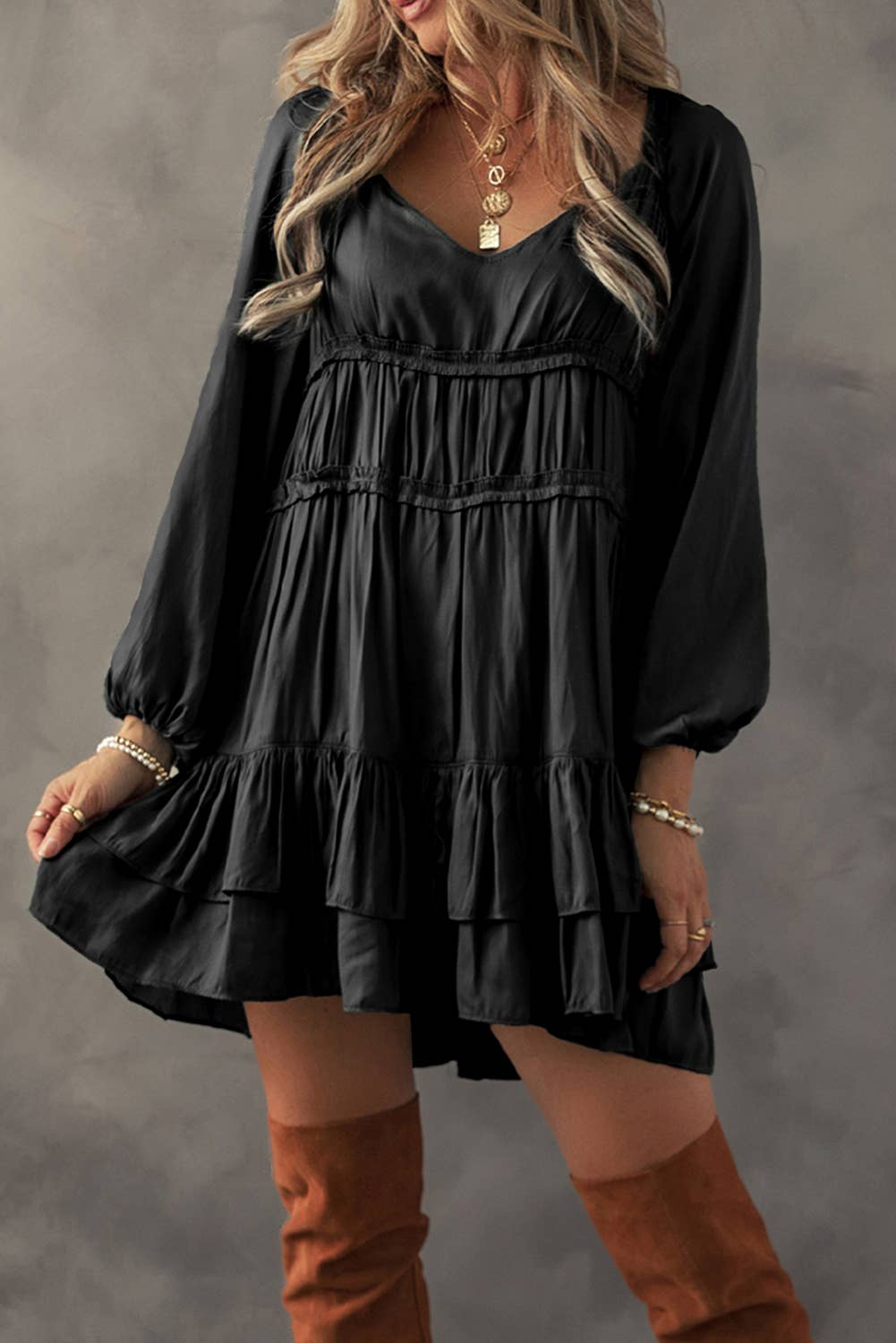 A woman wearing a black mini dress with tiered ruffles and puff sleeves, paired with brown boots.
