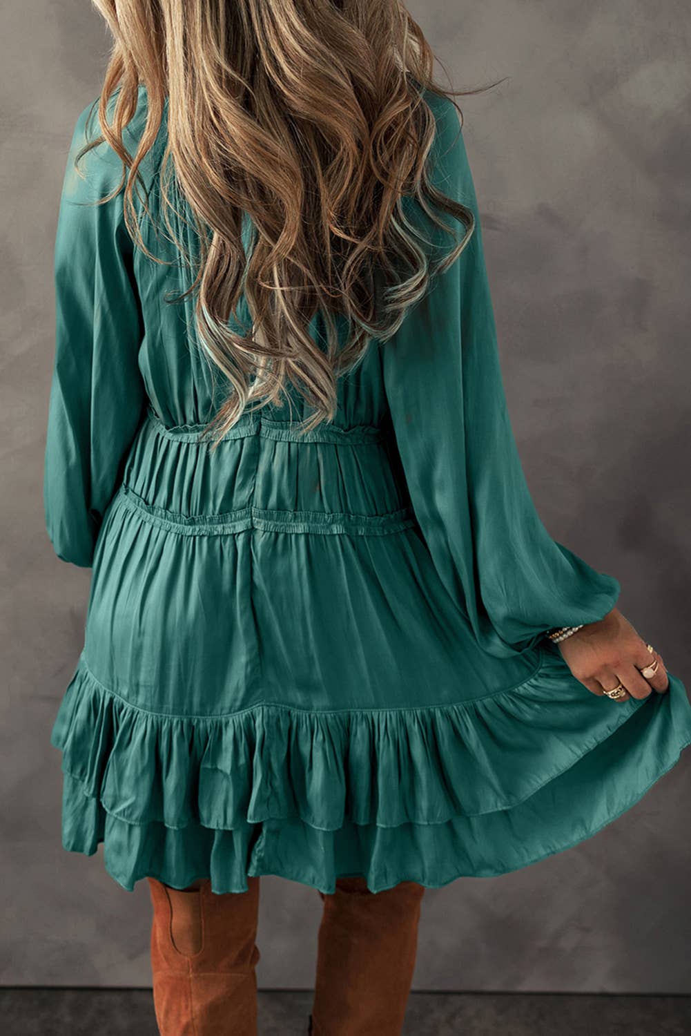 A woman wearing a green mini dress with tiered ruffles and puff sleeves, paired with brown boots.