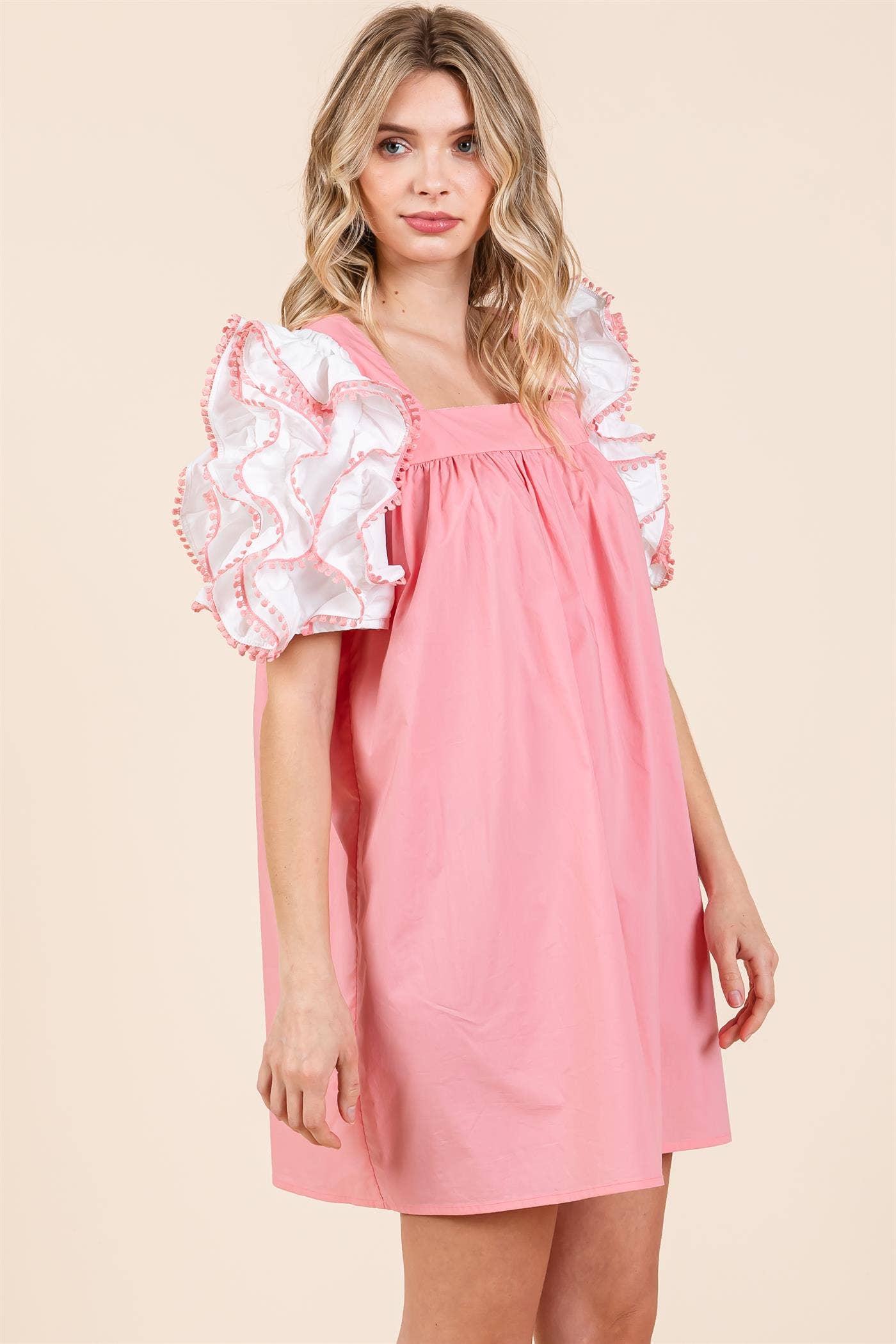 A model wearing a plus size babydoll mini dress with layered ruffled puff sleeves in a pink color.