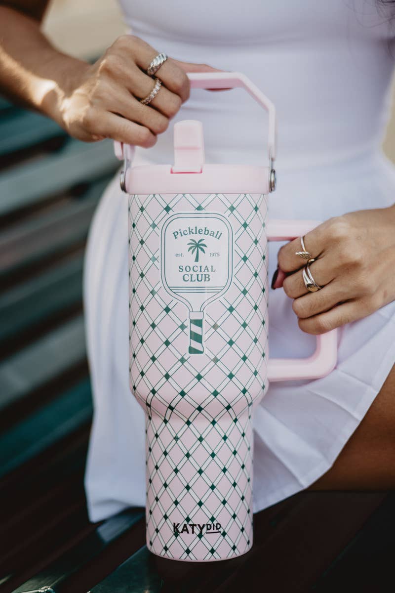A hand holding a pink and green plaid designed tumbler with a handle and a 'Pickleball Social Club' logo on it.