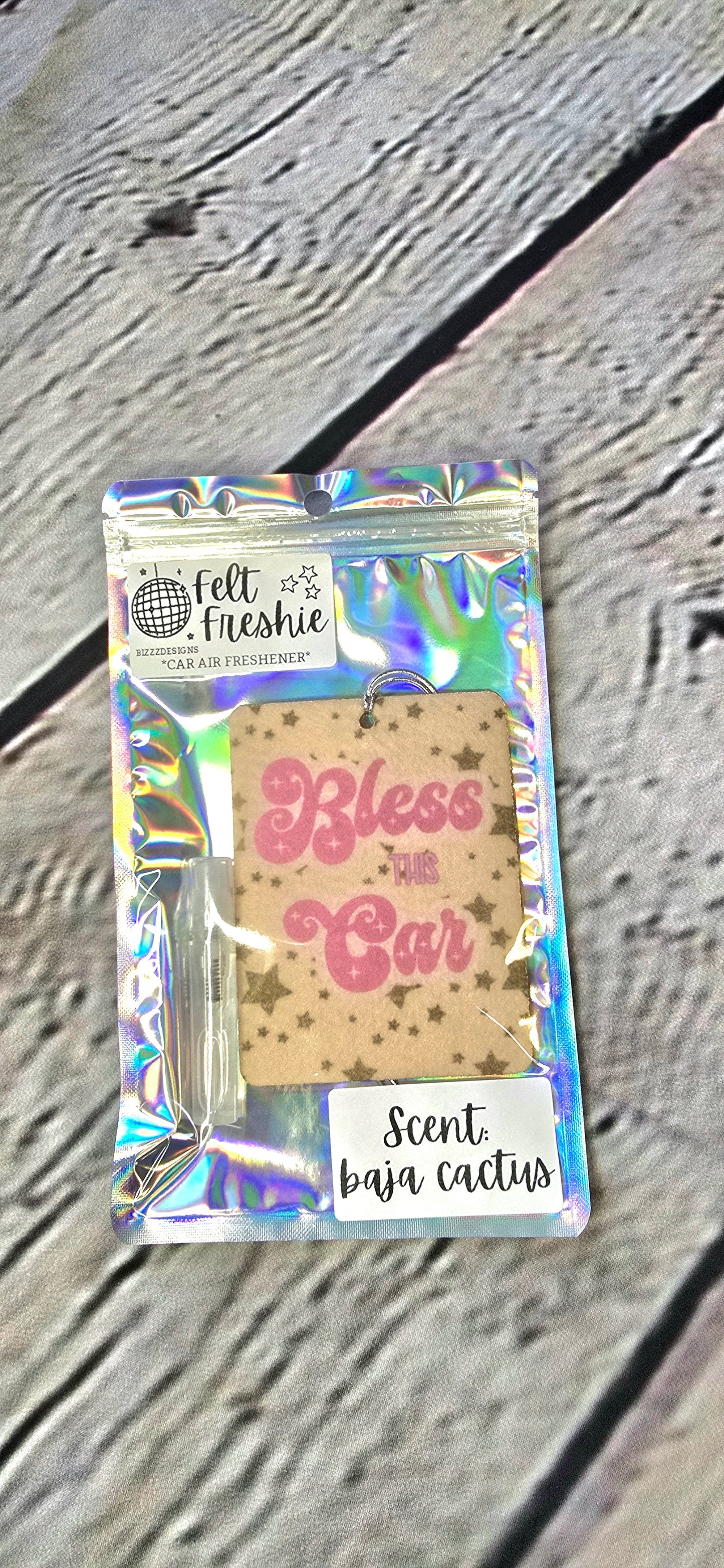 felt car air freshener with a 'Bless This Car' text and a small bottle of 'Summer Sunshine' scent, packaged in a clear, iridescent bag.