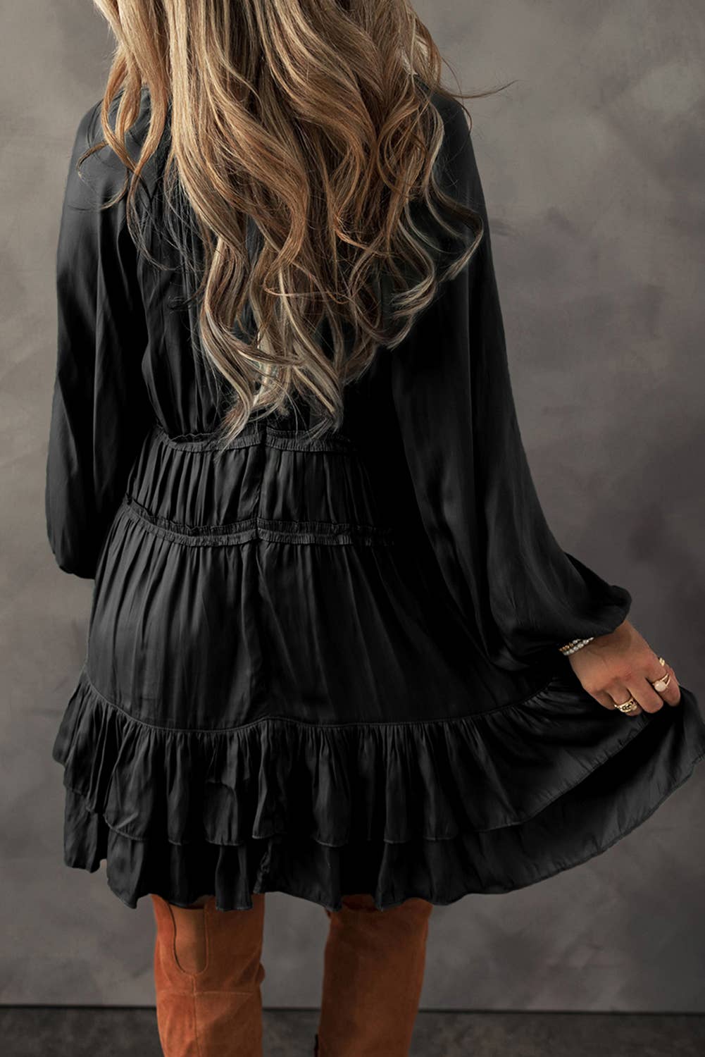 A woman wearing a black mini dress with tiered ruffles and puff sleeves, paired with brown boots.
