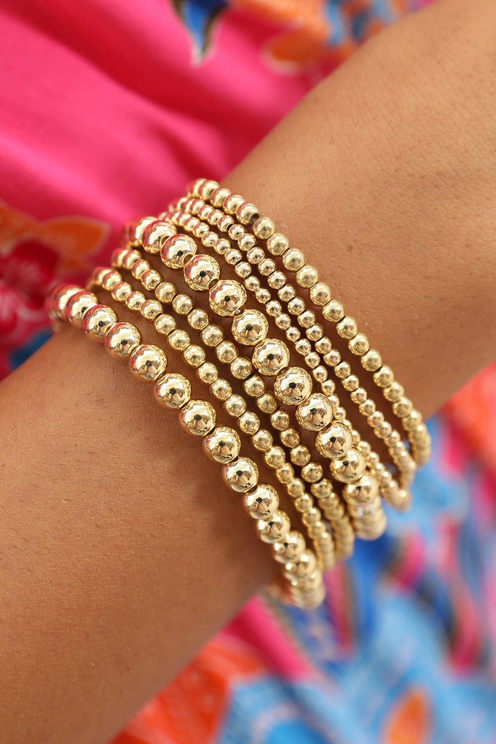 A set of seven gold-colored alloy bracelets with a beaded pattern displayed on a person's wrist.