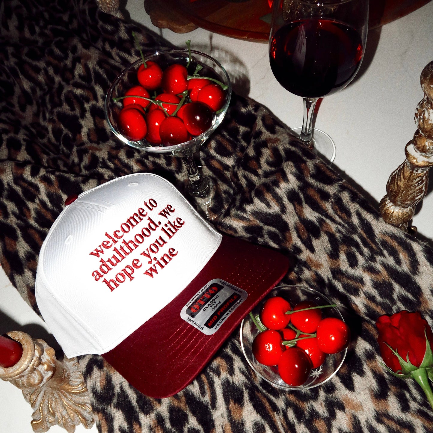 A maroon and white baseball cap with the text 'Welcome to adulthood.