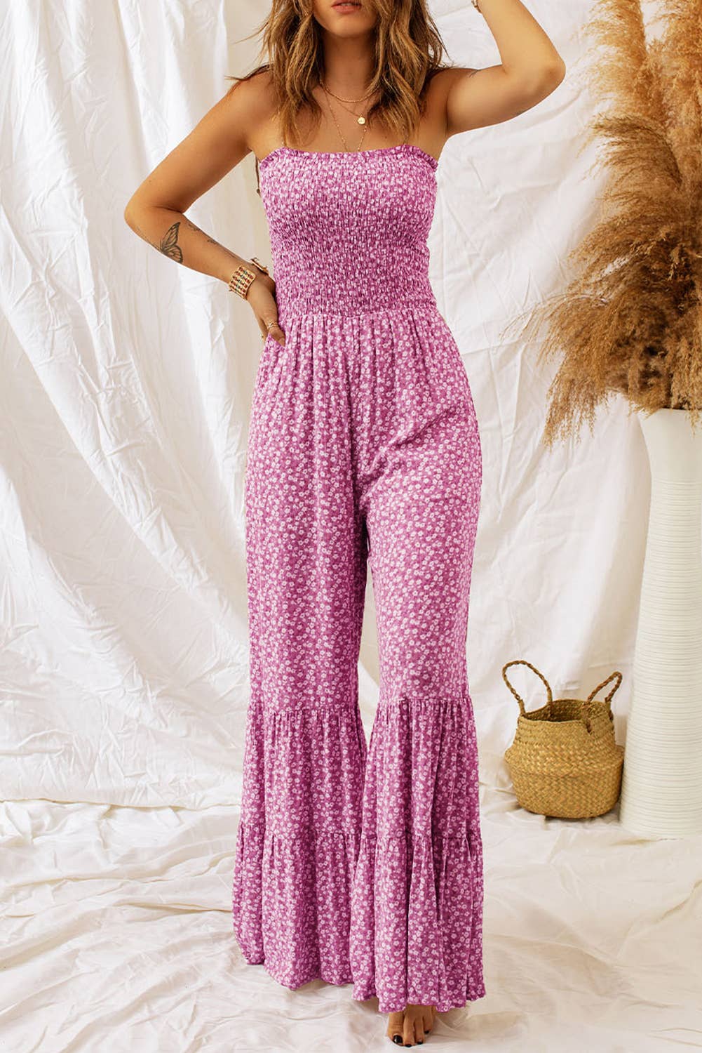 A woman wearing a purple floral jumpsuit with wide legs and spaghetti straps.