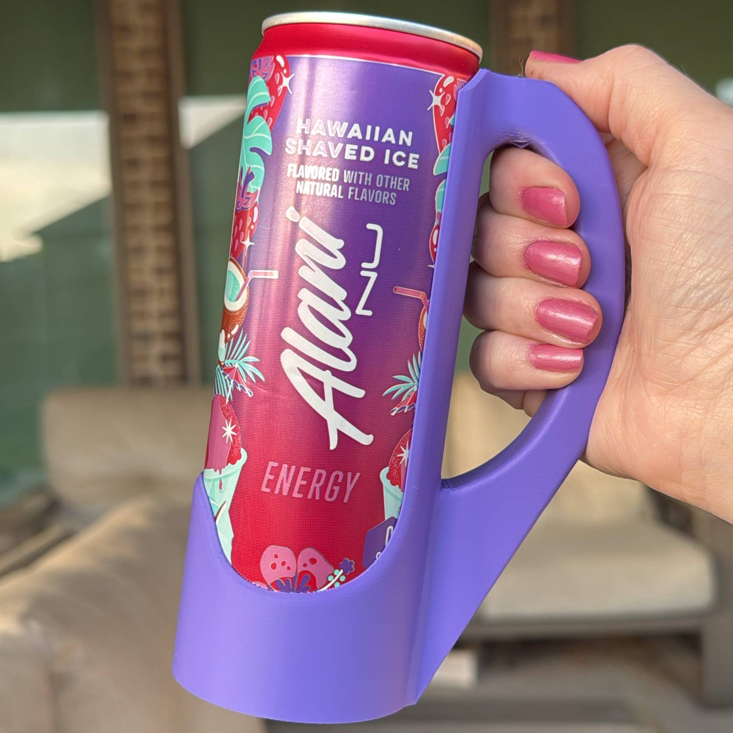 A hand holding a purple skinny can handle with a colorful can labeled 'Aloha Energy' in the background.