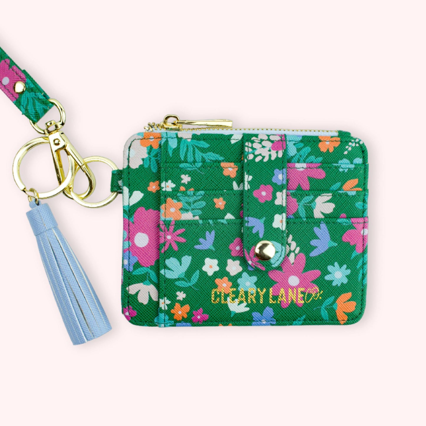 A hand holding a green wallet keychain with a floral pattern and gold hardware. The keychain is attached to a strap and there are multiple keys on it.