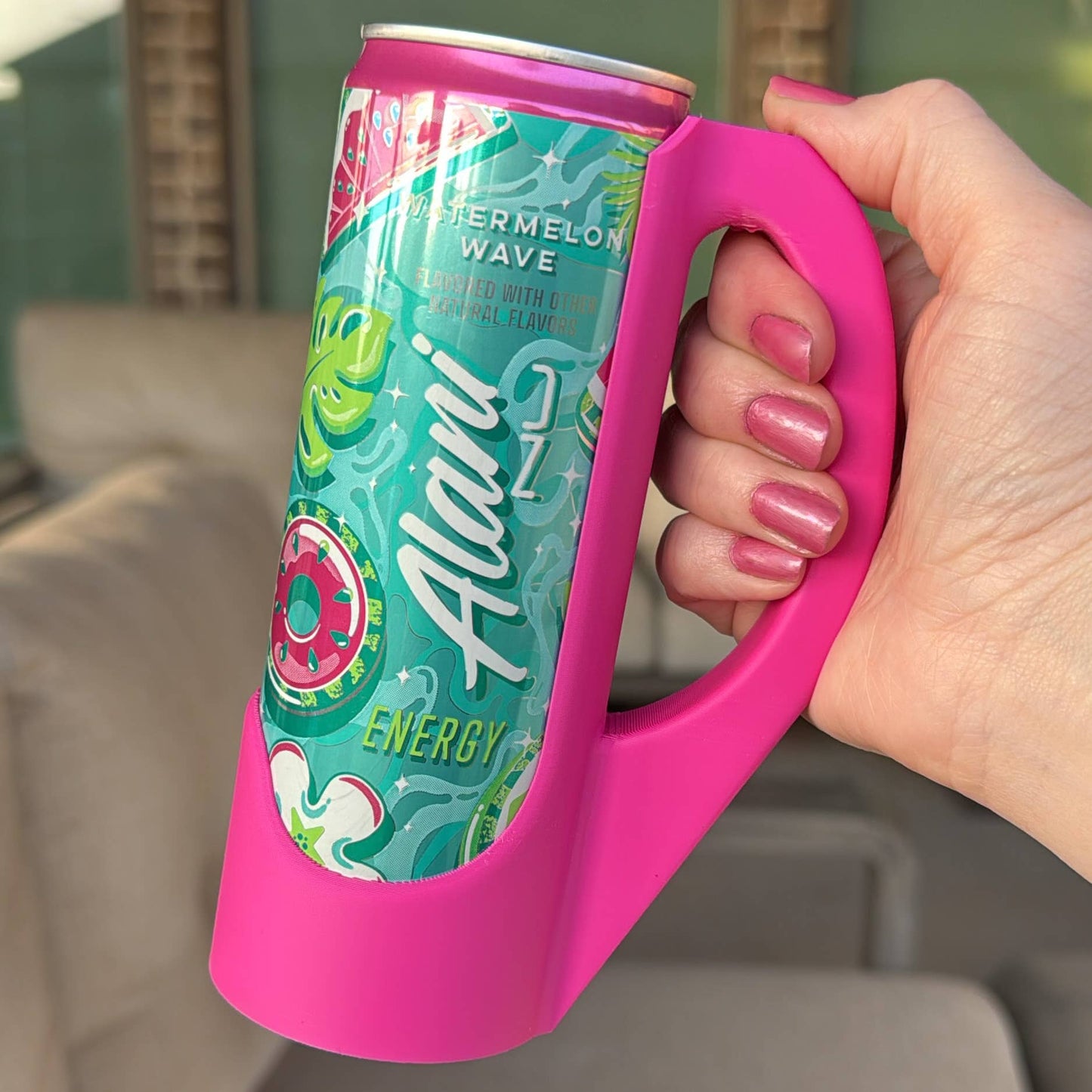 A hand holding a purple skinny can handle with a colorful can labeled 'Aloha Energy' in the background.