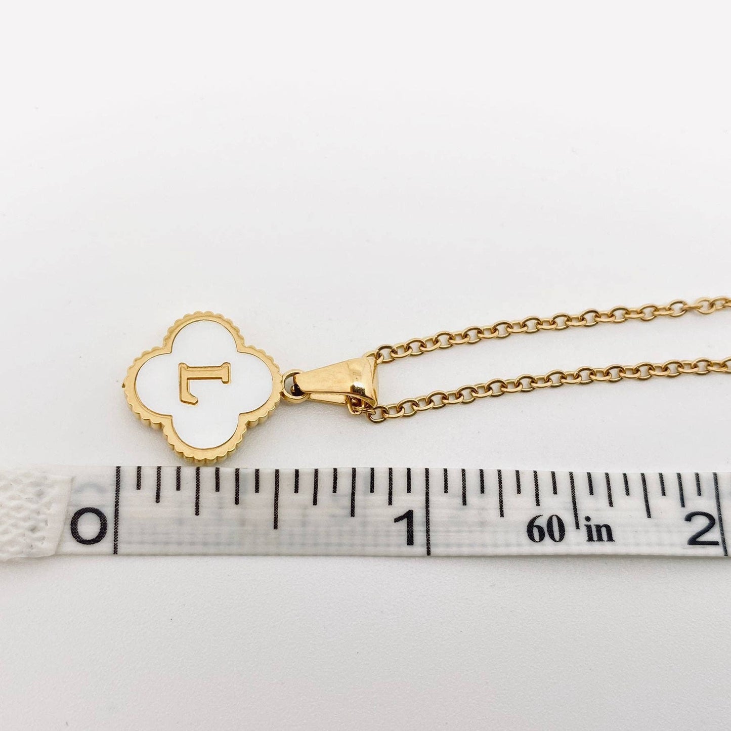 Gold necklace with a clover-shaped pendant on a ruler for scale