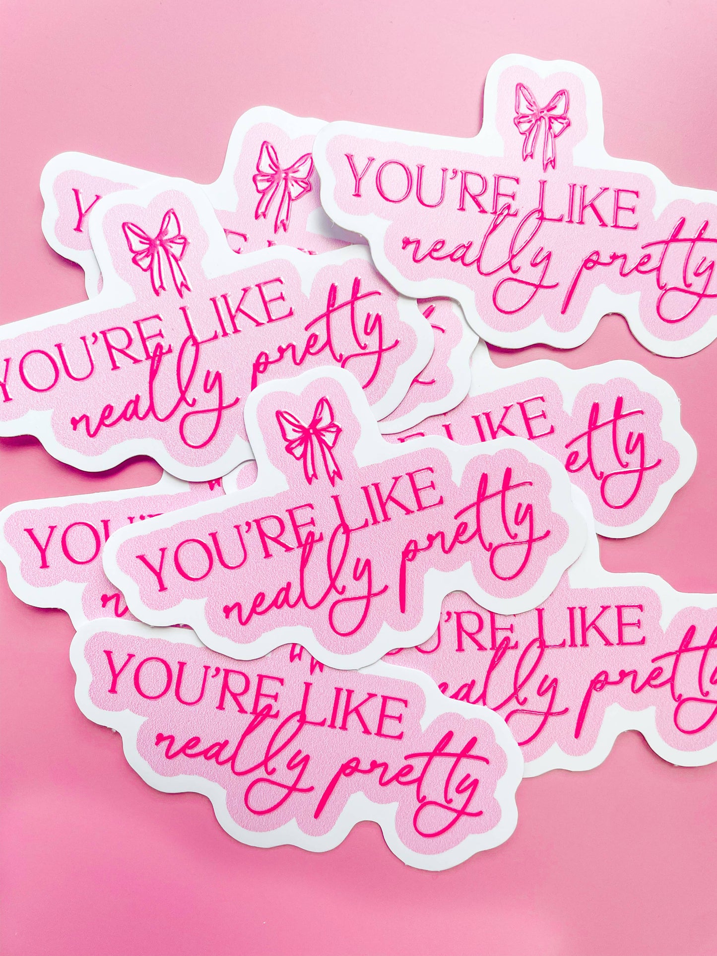 A collection of pink stickers with the phrase 'YOU'RE LIKE REALLY PRETTY' printed in a cursive and playful font, adorned with small heart and arrow illustrations.