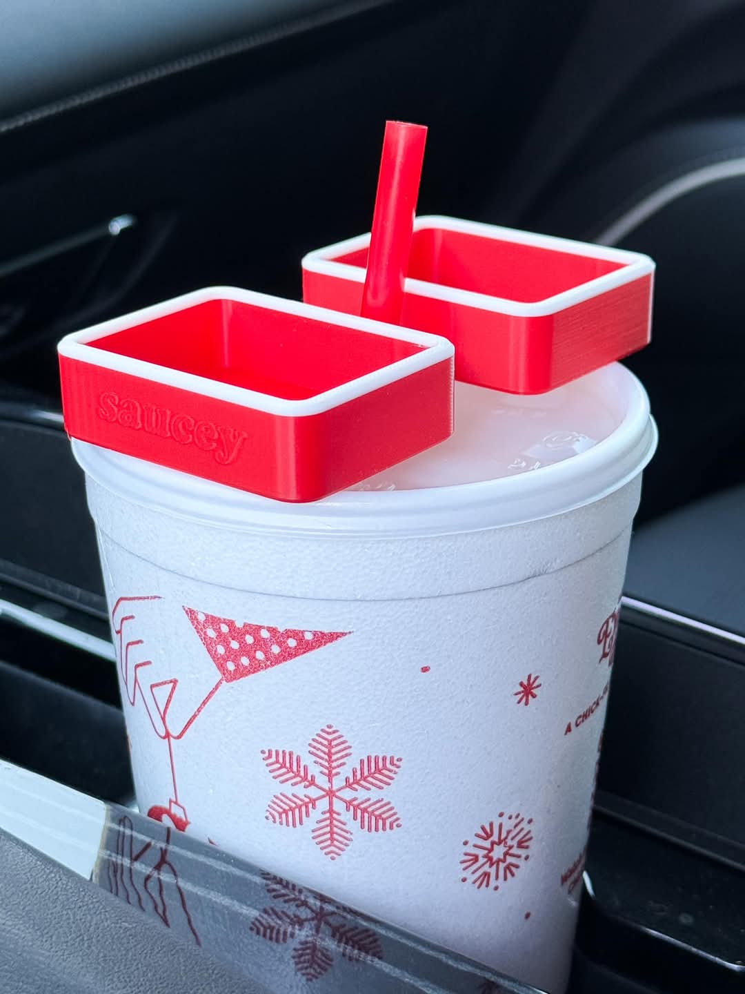 A red Saucey Dipping Sauce Holder attached to a white cup with holiday-themed designs, containing a red straw.