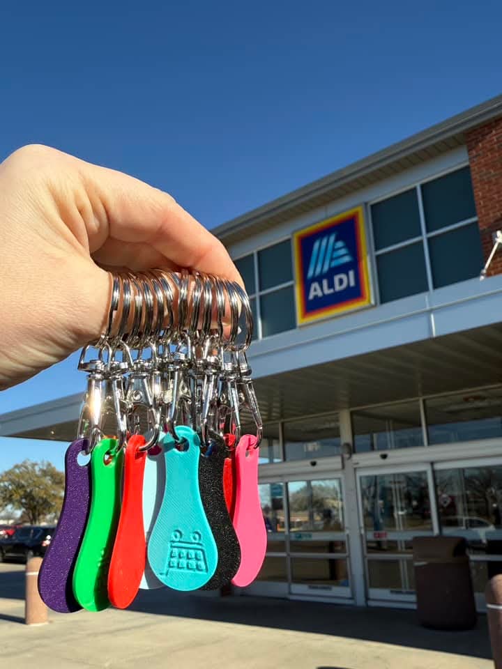 A hand holding a keychain with multiple keys attached, displayed in front of an Aldi supermarket.
