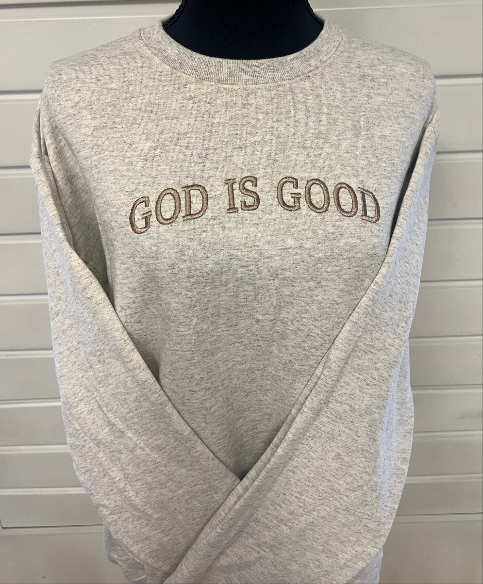 A gray sweatshirt with the phrase 'GOD IS GOOD' embroidered across the chest in capital letters.