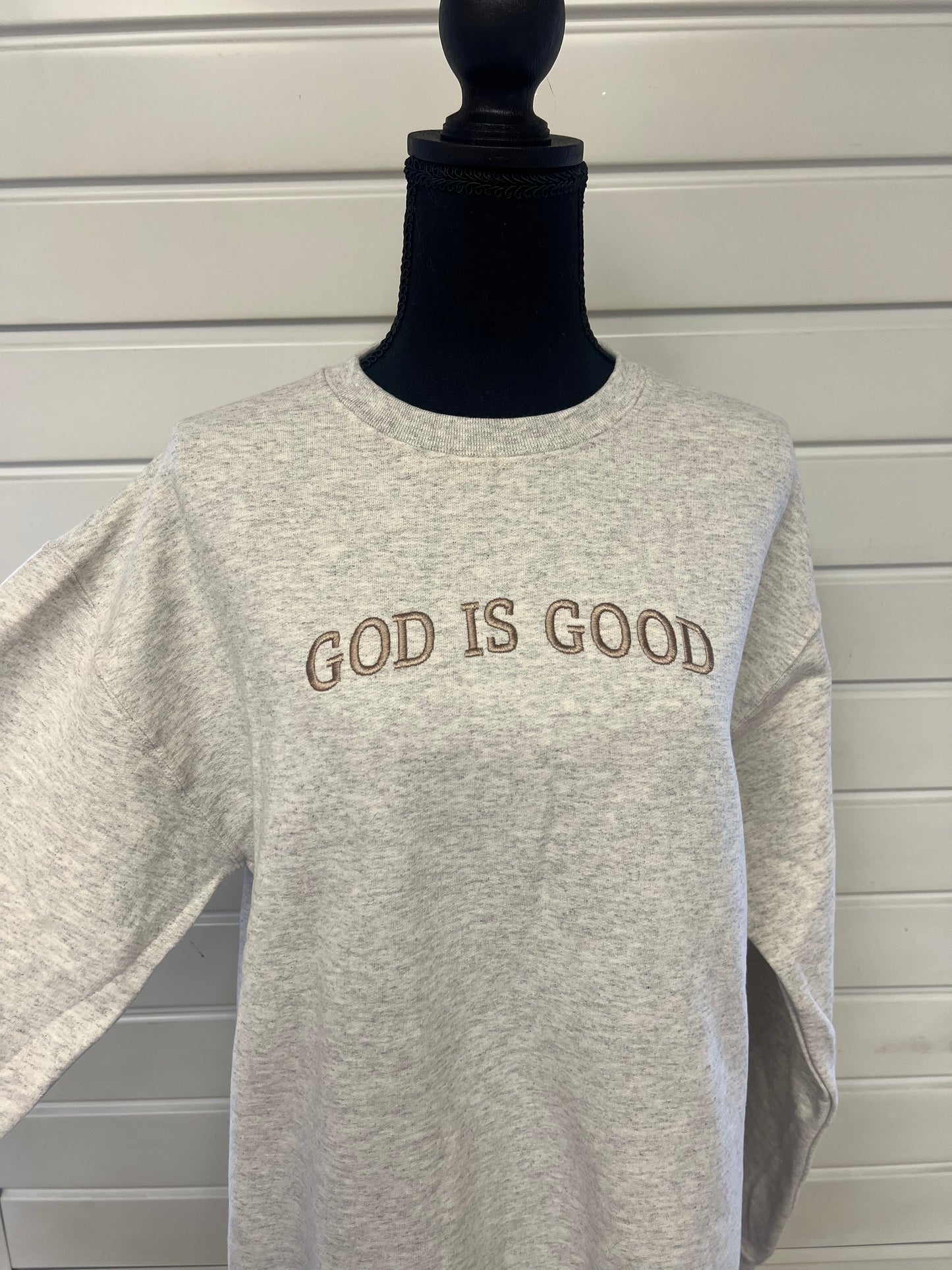 A gray sweatshirt with the phrase 'GOD IS GOOD' embroidered across the chest in capital letters.