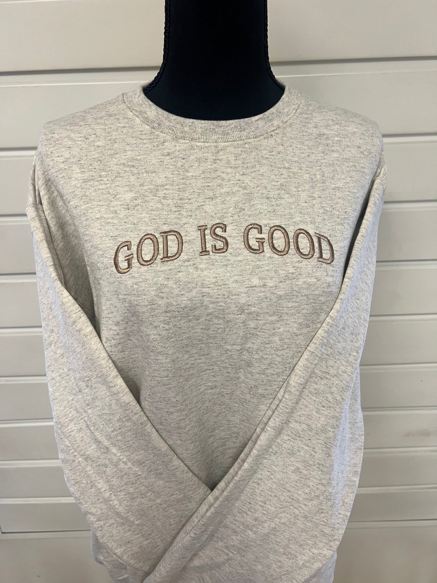 A gray sweatshirt with the phrase 'GOD IS GOOD' embroidered across the chest in capital letters.