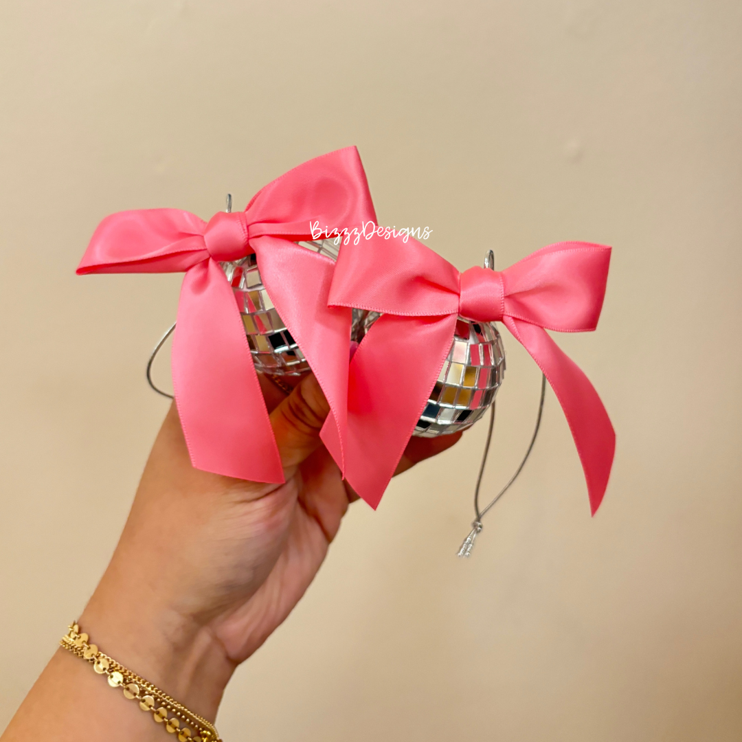 a hand holding two disco ball car charms with a pink ribbon