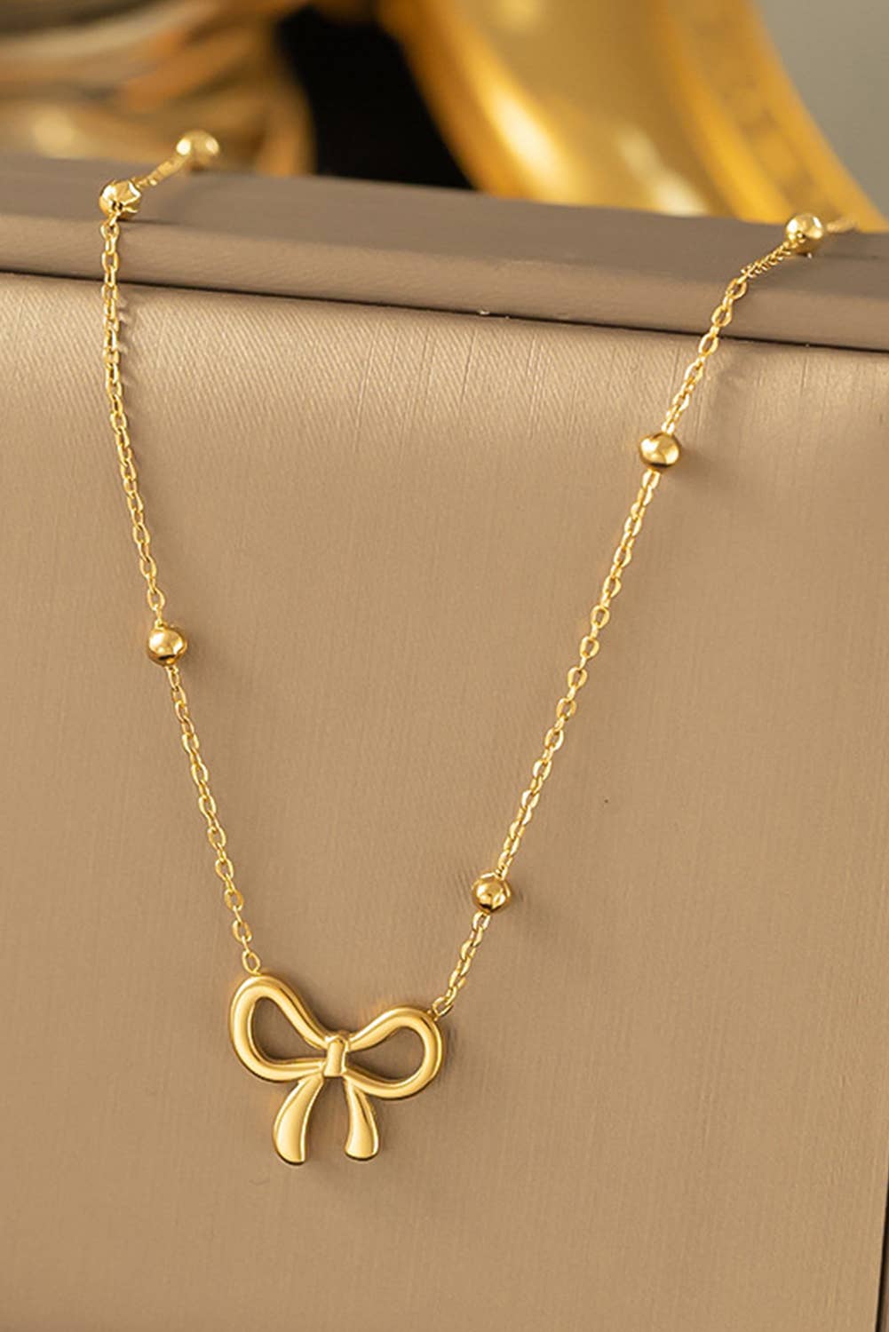 A gold-colored bowknot pendant choker necklace laid out on a surface.