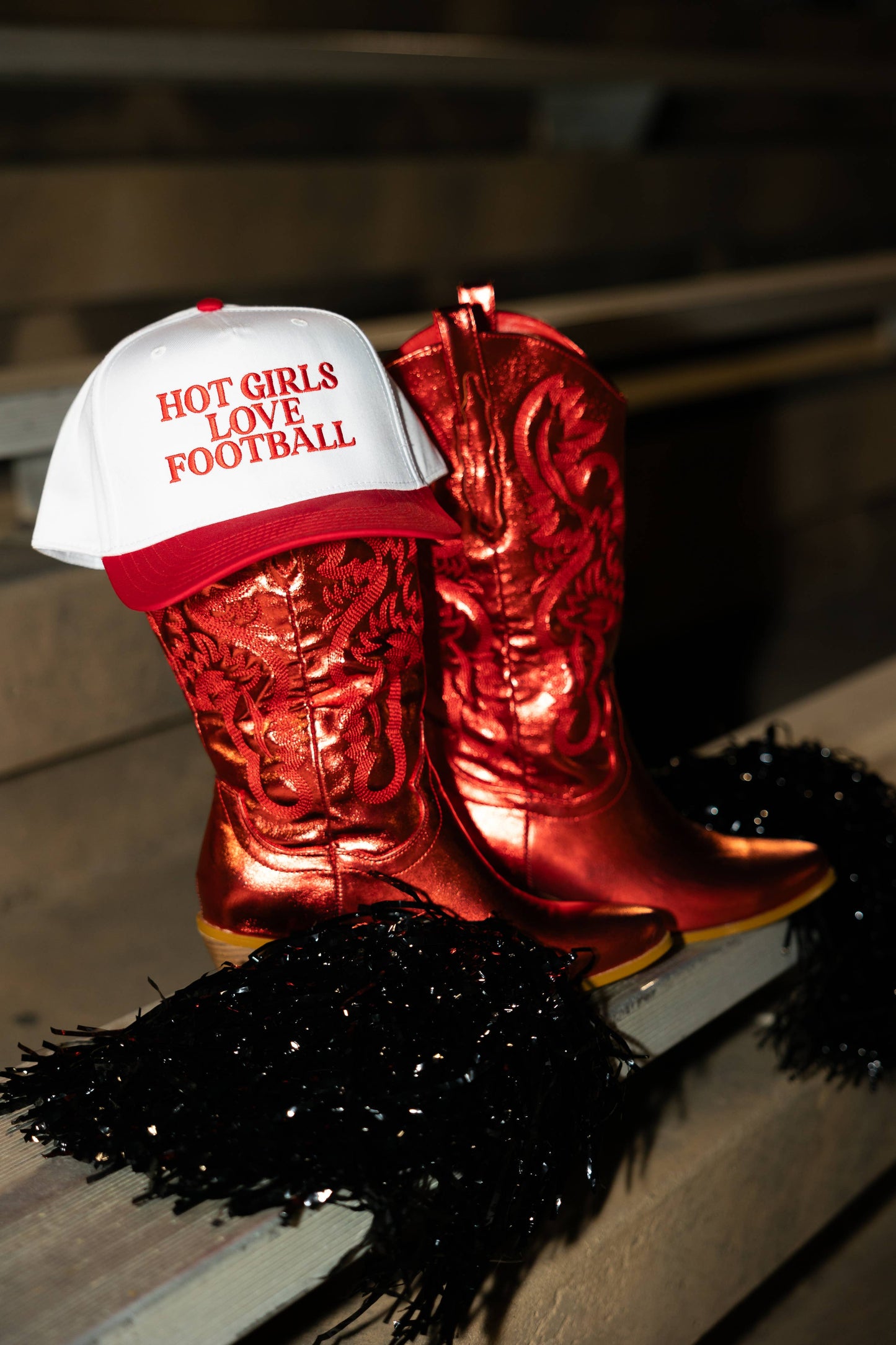 Trucker hat with Hot girls love football embroidered in red propped on a pair of red metallic cowboy boots