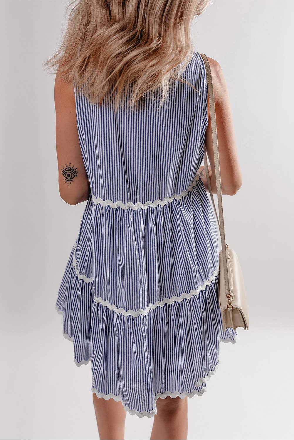 A sleeveless mini dress with horizontal stripes and lace trim detailing, in blue and white, worn by a person.