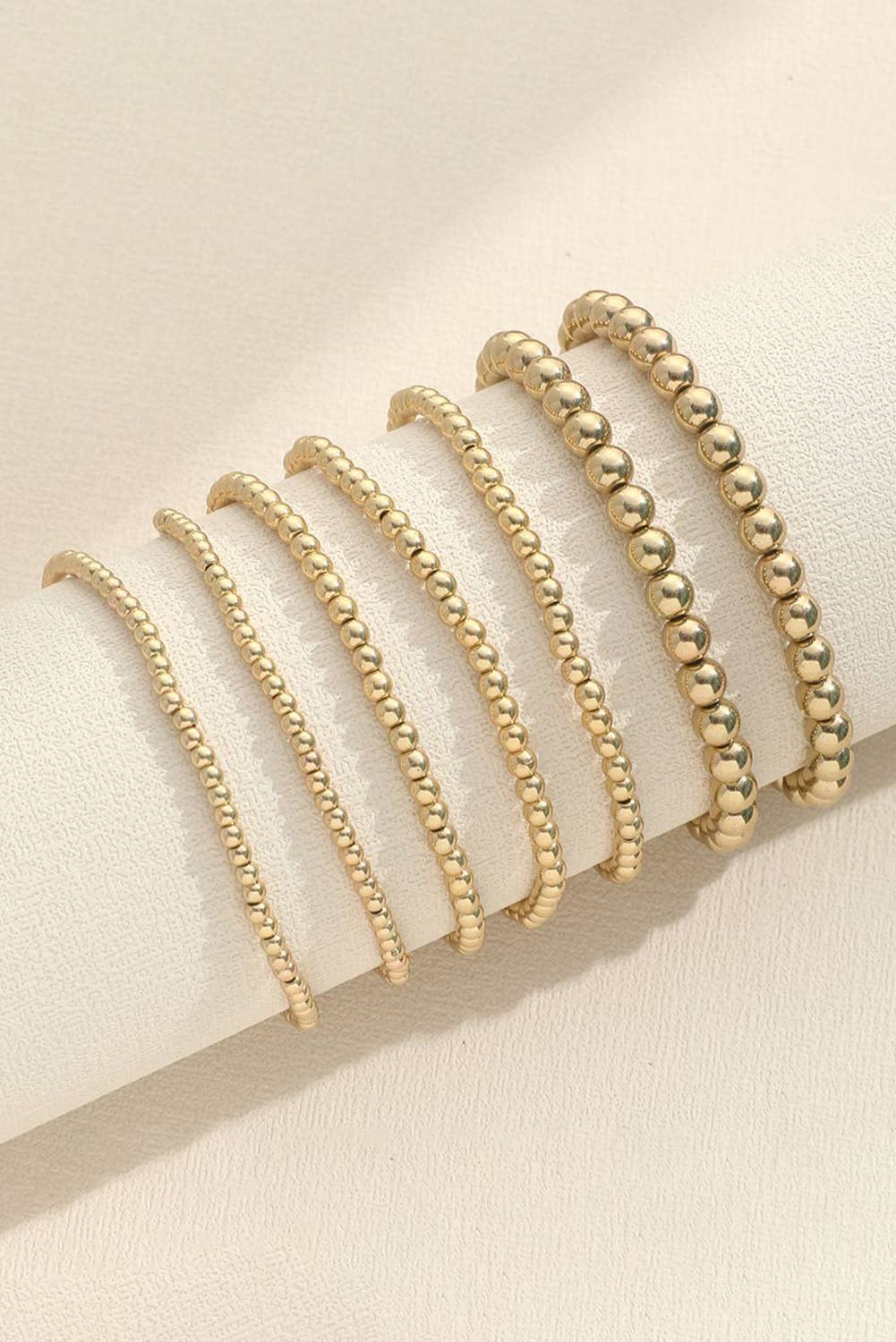 A set of seven gold-colored alloy bracelets with a beaded pattern displayed on a jewelry display smallest to largest