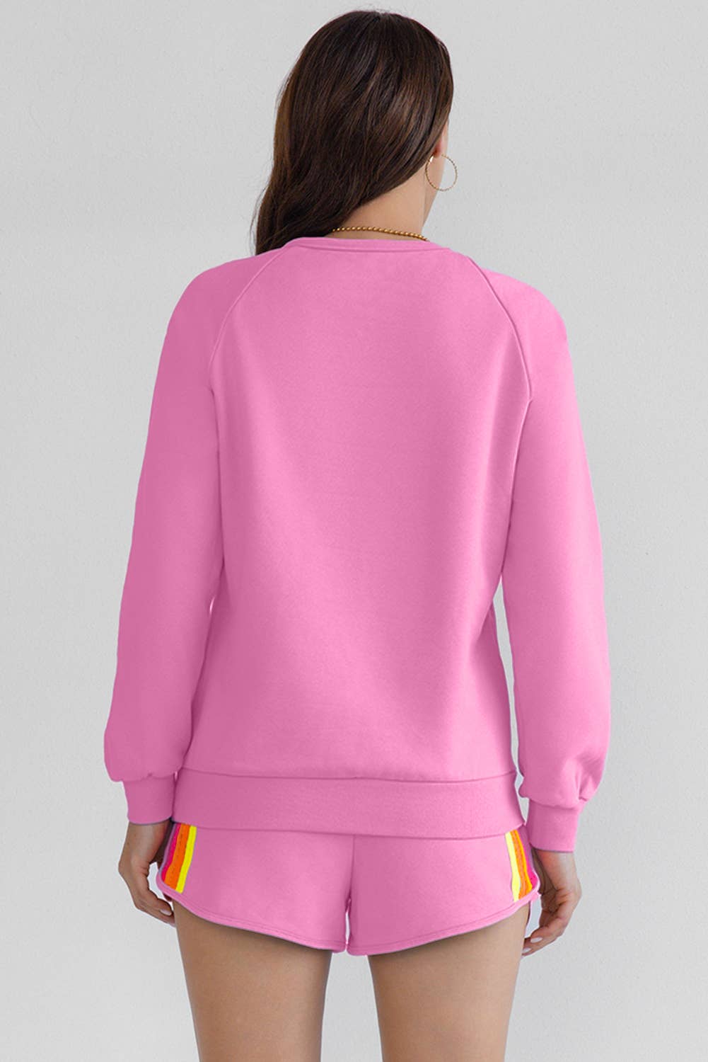 A woman wearing a long sleeve top and shorts set in pink with color contrast trim, standing in a room with light-colored walls.