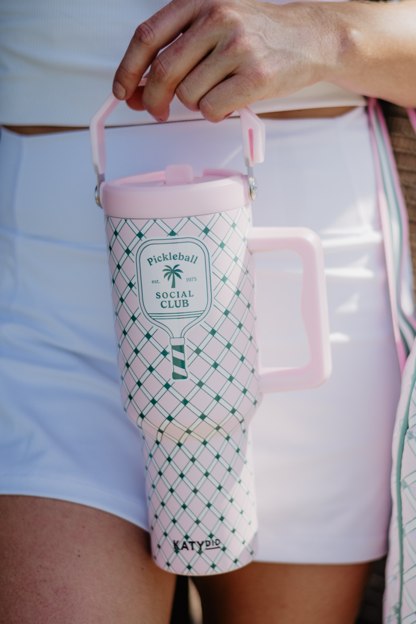 A hand holding a pink and green plaid designed tumbler with a handle and a 'Pickleball Social Club' logo on it.