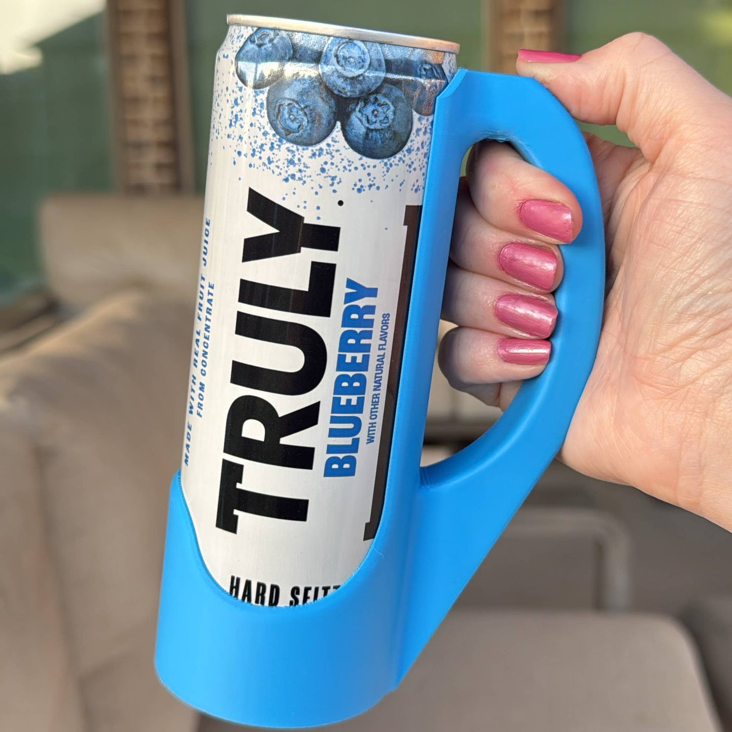 A hand holding a purple skinny can handle with a colorful can labeled 'Aloha Energy' in the background.