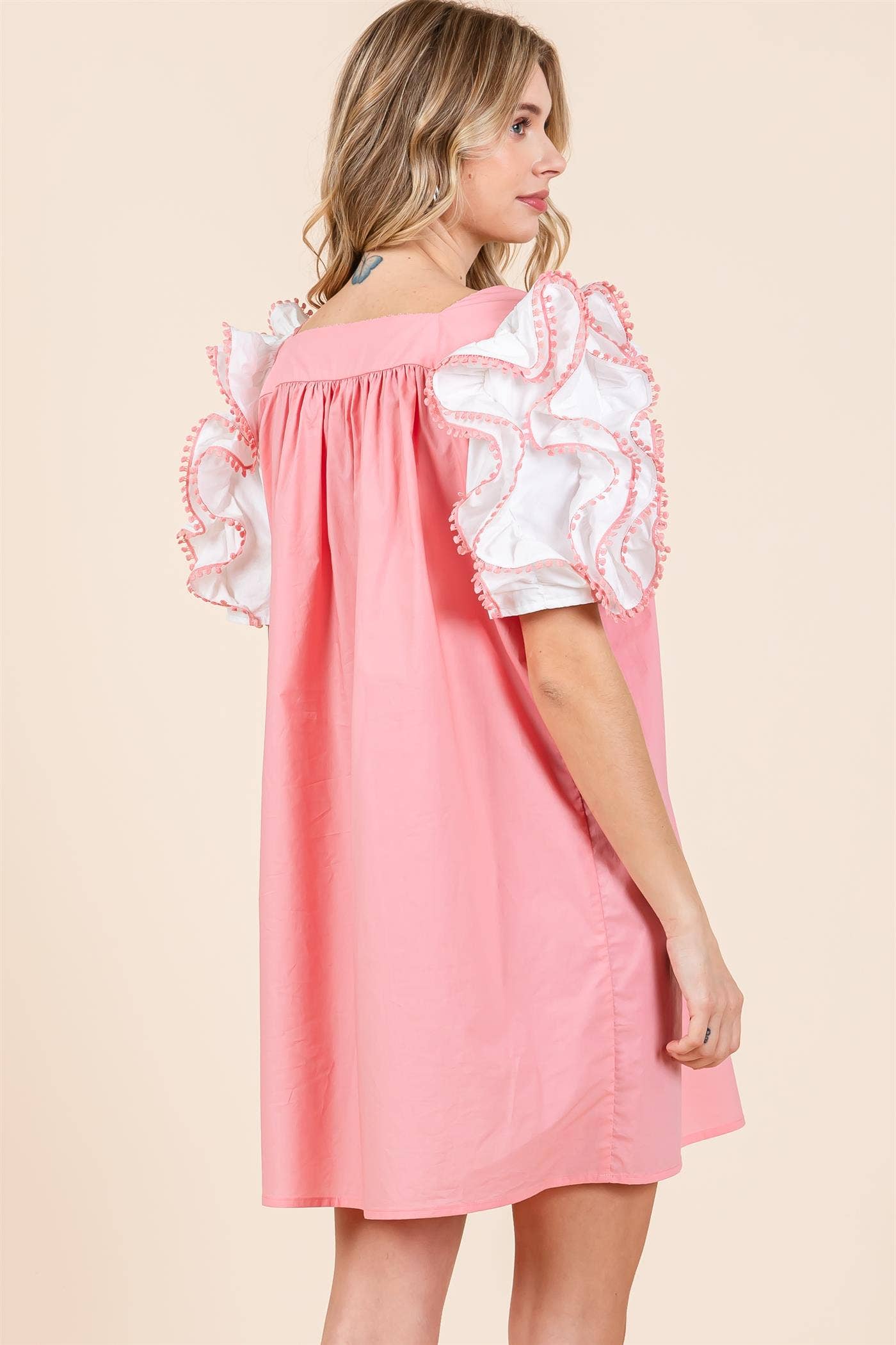A model wearing a plus size babydoll mini dress with layered ruffled puff sleeves in a pink color.