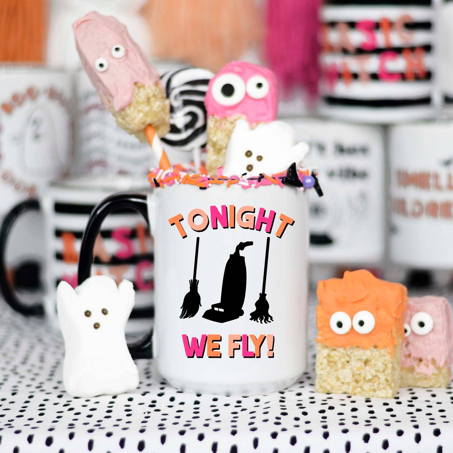 Halloween-themed mug with decorative treats on a polka dot tablecloth.