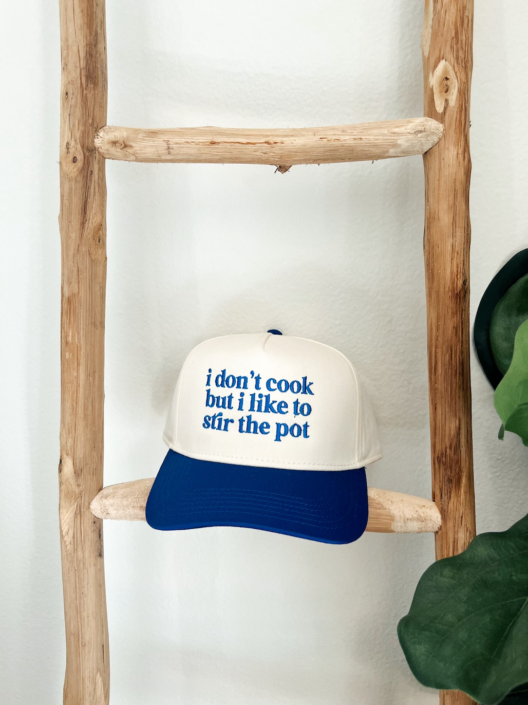 blue and white trucker hat with the text 'i don't cook but i like to stir the pot' embroidered on the front.