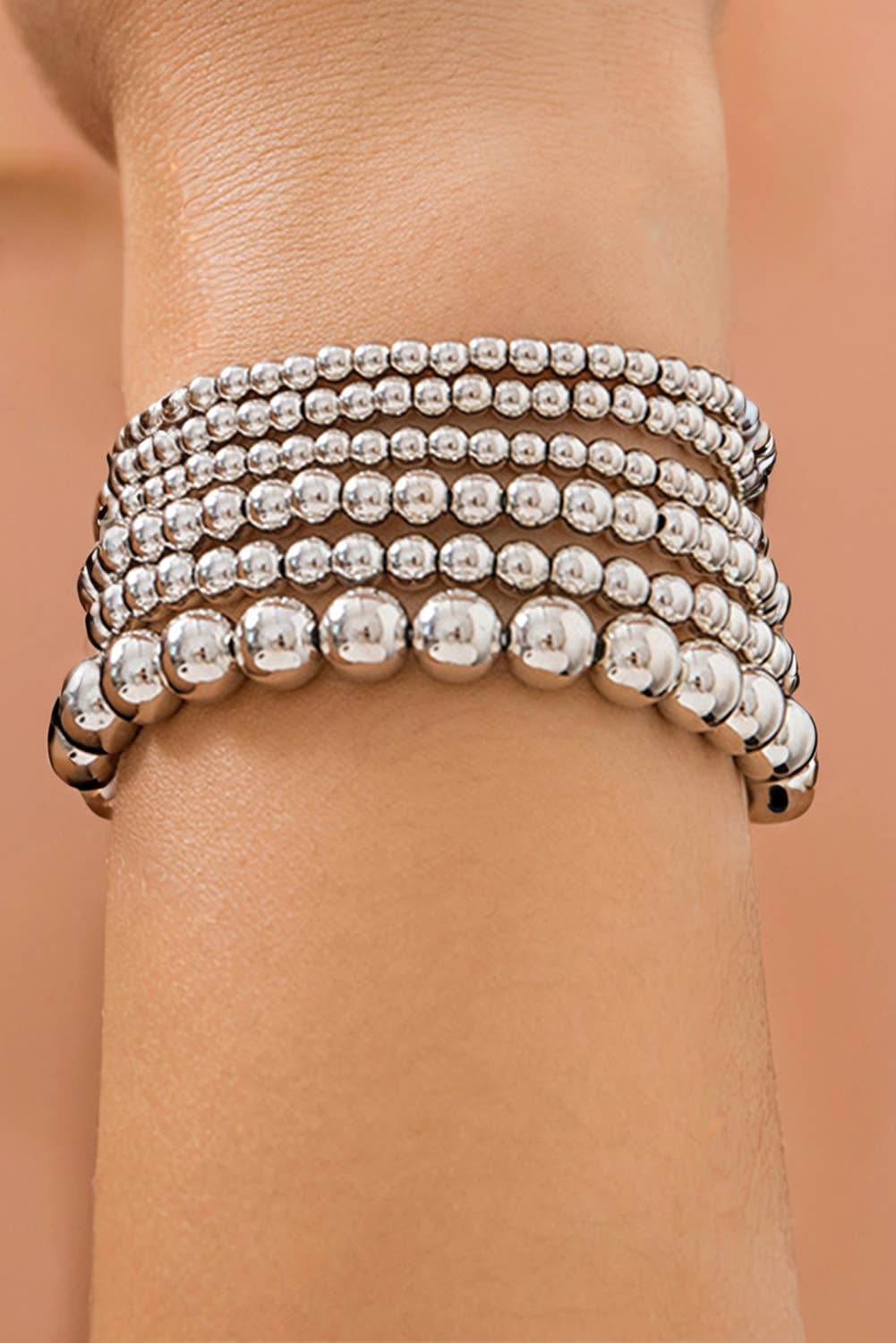 A close-up image of a multilayered silver beaded bracelet on a person's wrist.