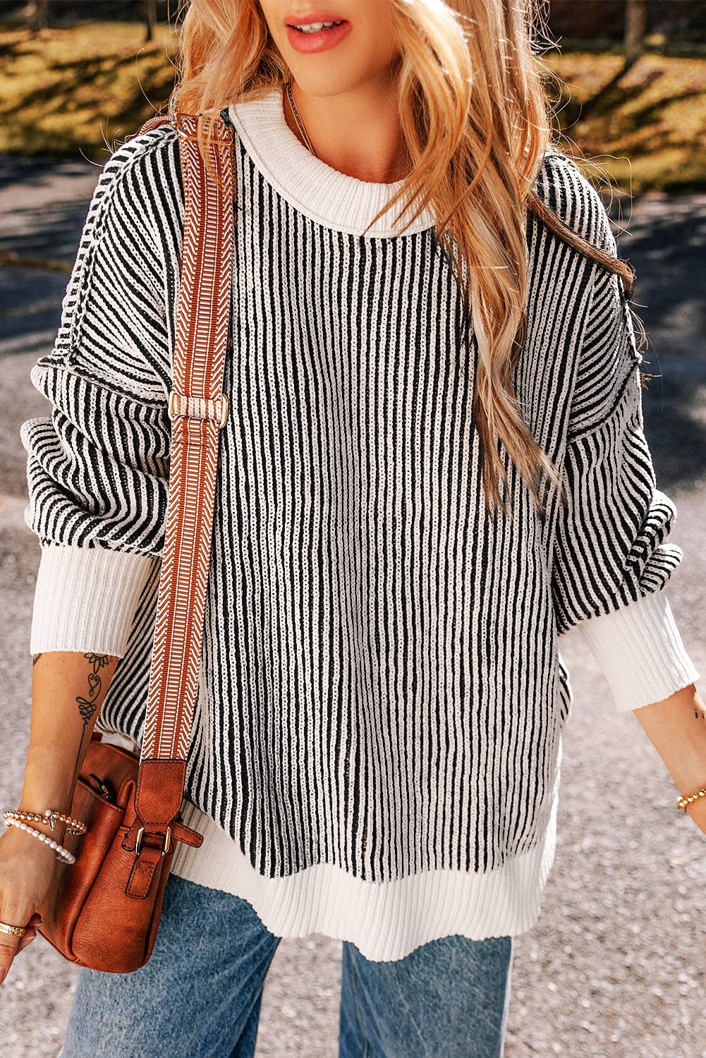 A woman wearing a striped contrast trim loose sweater in black and white, paired with blue jeans and a brown bag.