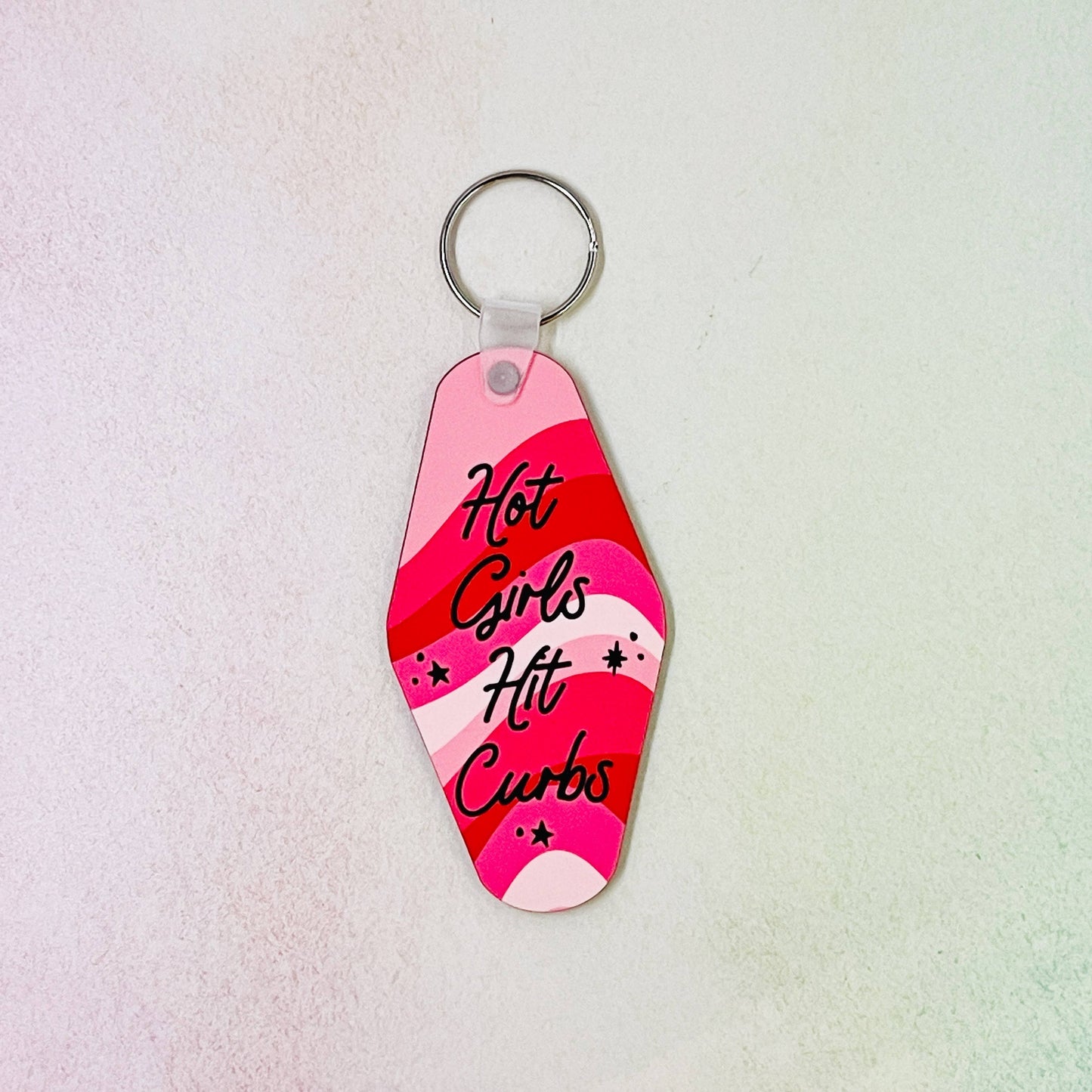 A keychain with a double-sided design featuring text 'Hot Girls Hit Curbs' on a pink and red background.