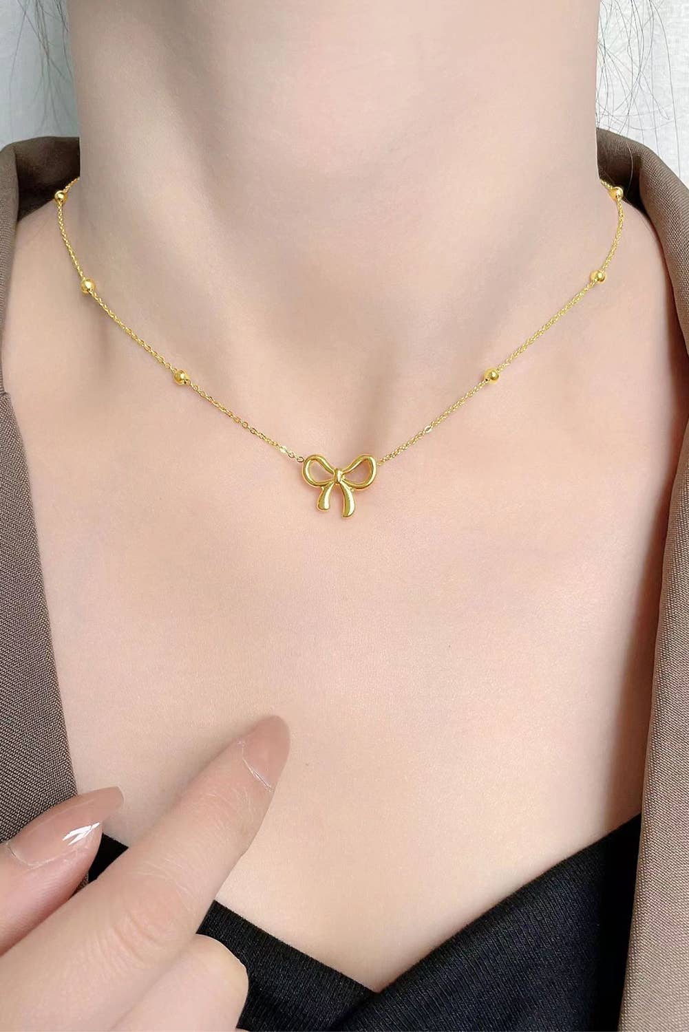 A gold-colored bowknot pendant choker necklace displayed on a persons neck line