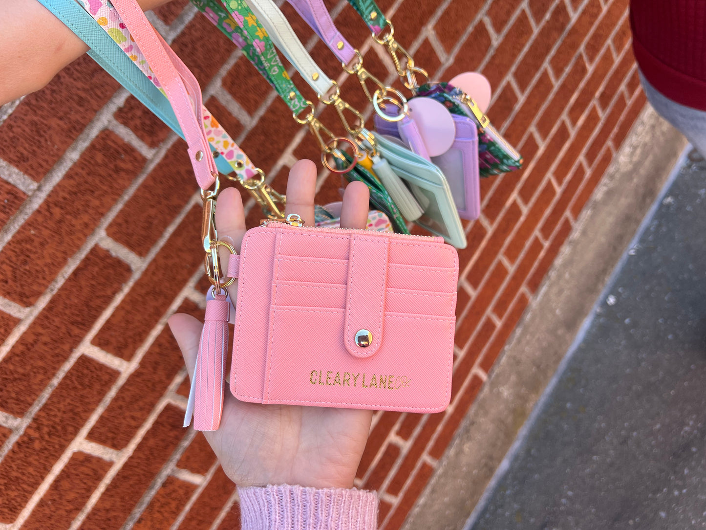 A person holding a pink wallet keychain with multiple keys in a colorful strap, against a brick wall background.
