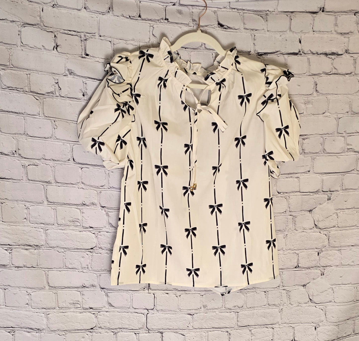 a white ruffled bubble sleeve notched neck blouse with a black pattern against a white wash brick wall