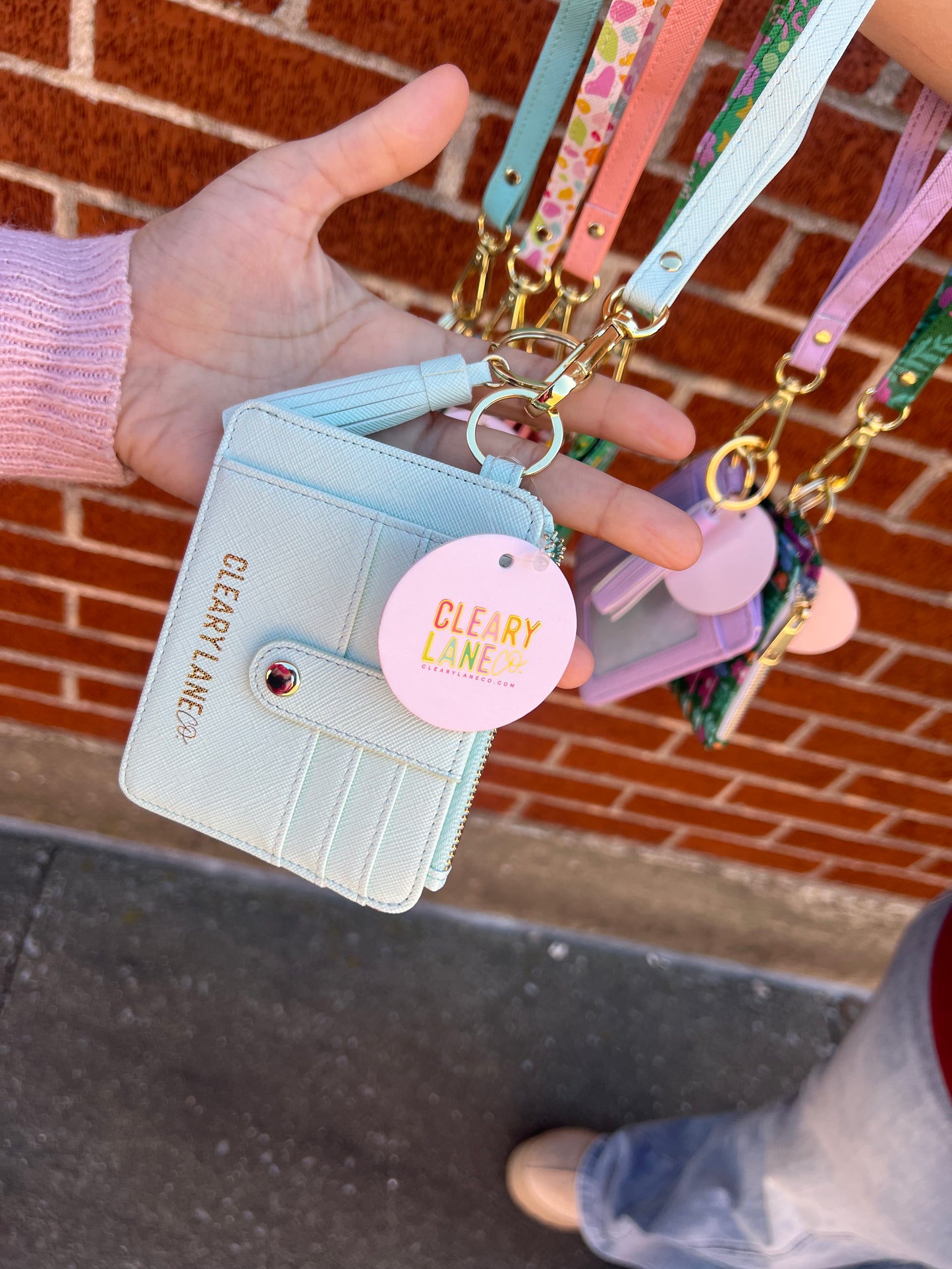 A hand holding a mint green wallet keychain with a zippered pouch and a key ring, displayed in a variety of colors.