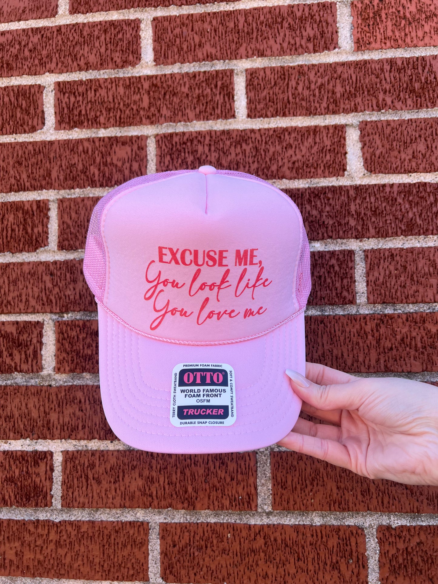 A pink trucker hat with the phrase 'You Look Like You Love Me' printed in pink and orange colors on the front.