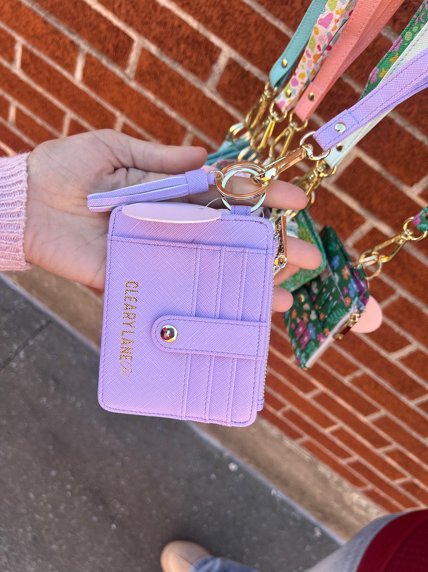A hand holding a lilac-colored wallet keychain with a sturdy key ring and a zippered pouch, featuring gold hardware.