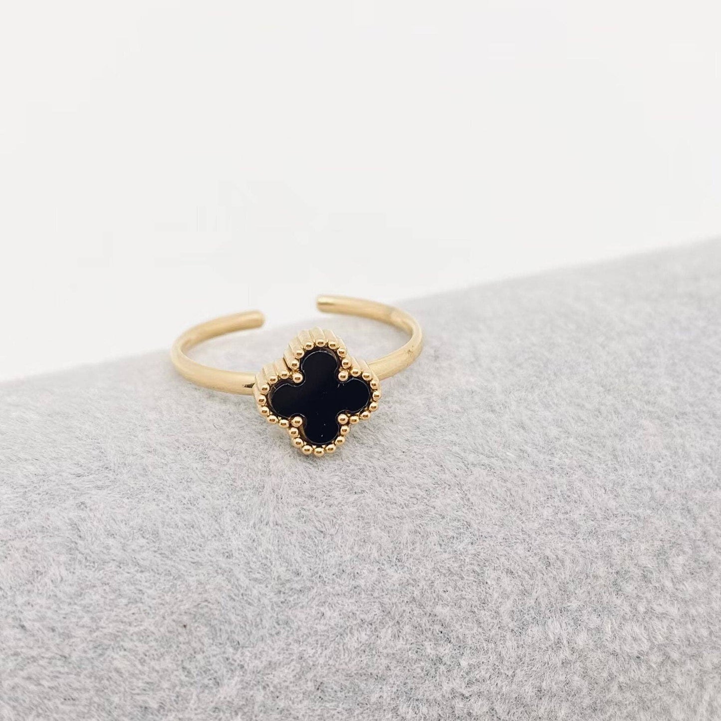 Gold ring with a black clover-shaped center on a gray surface