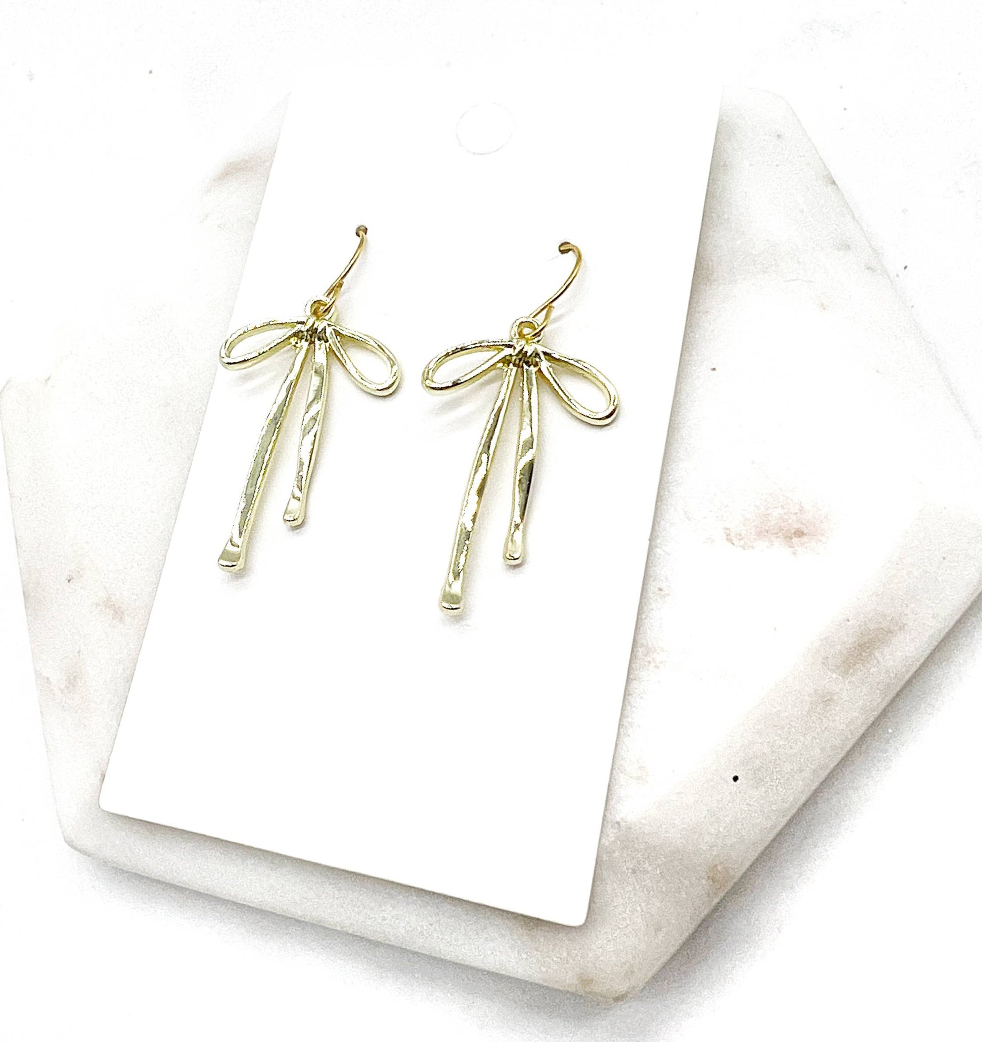 Gold bow-shaped earrings on a white card with a marble surface