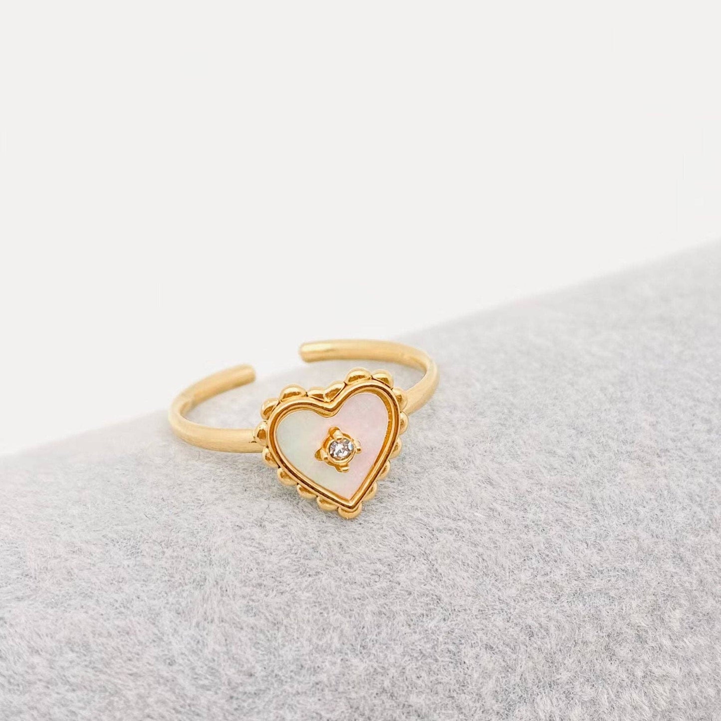 Gold heart-shaped ring with a small diamond on a light gray surface