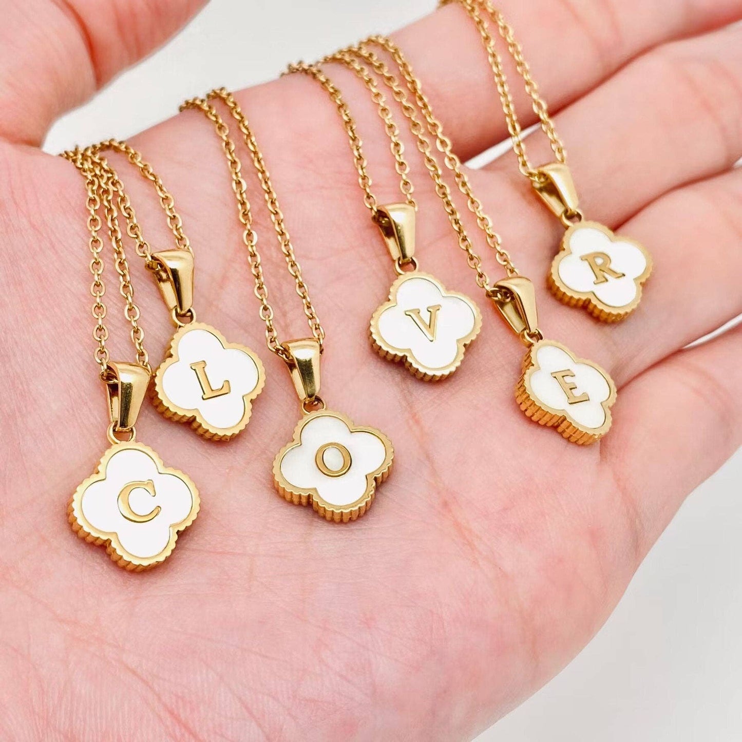 Gold necklaces with clover-shaped pendants displaying letters on a hand.