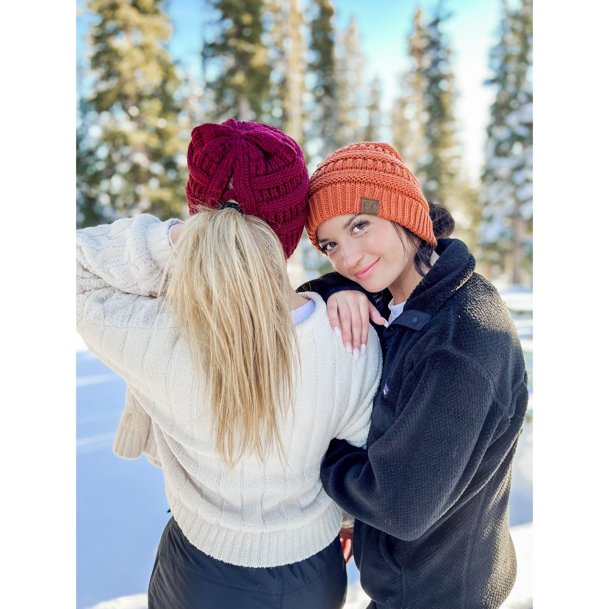 Two people in winter clothing with colorful beanies standing in a snowy landscape.