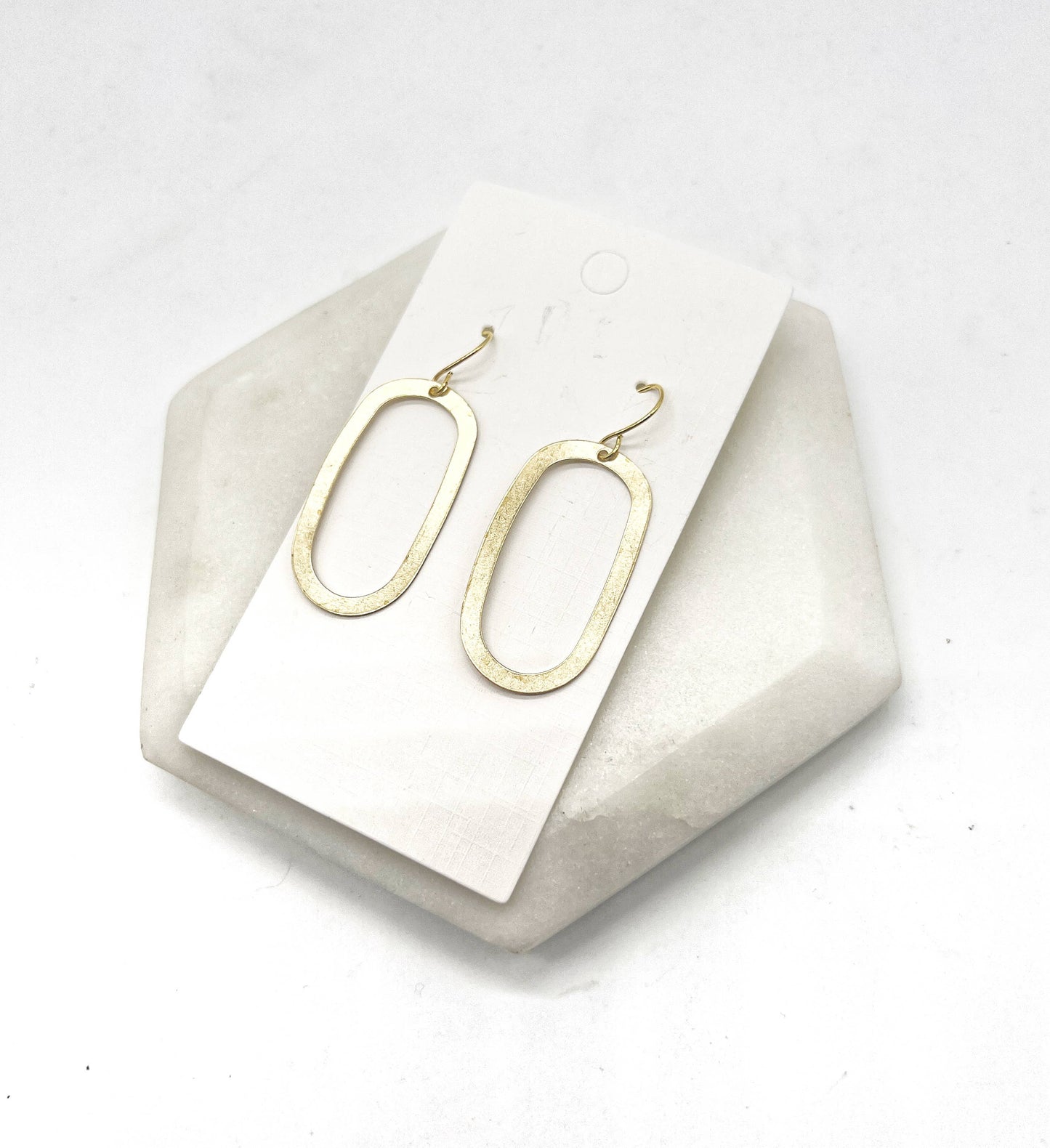 Gold oval earrings on a white card with a geometric stone base