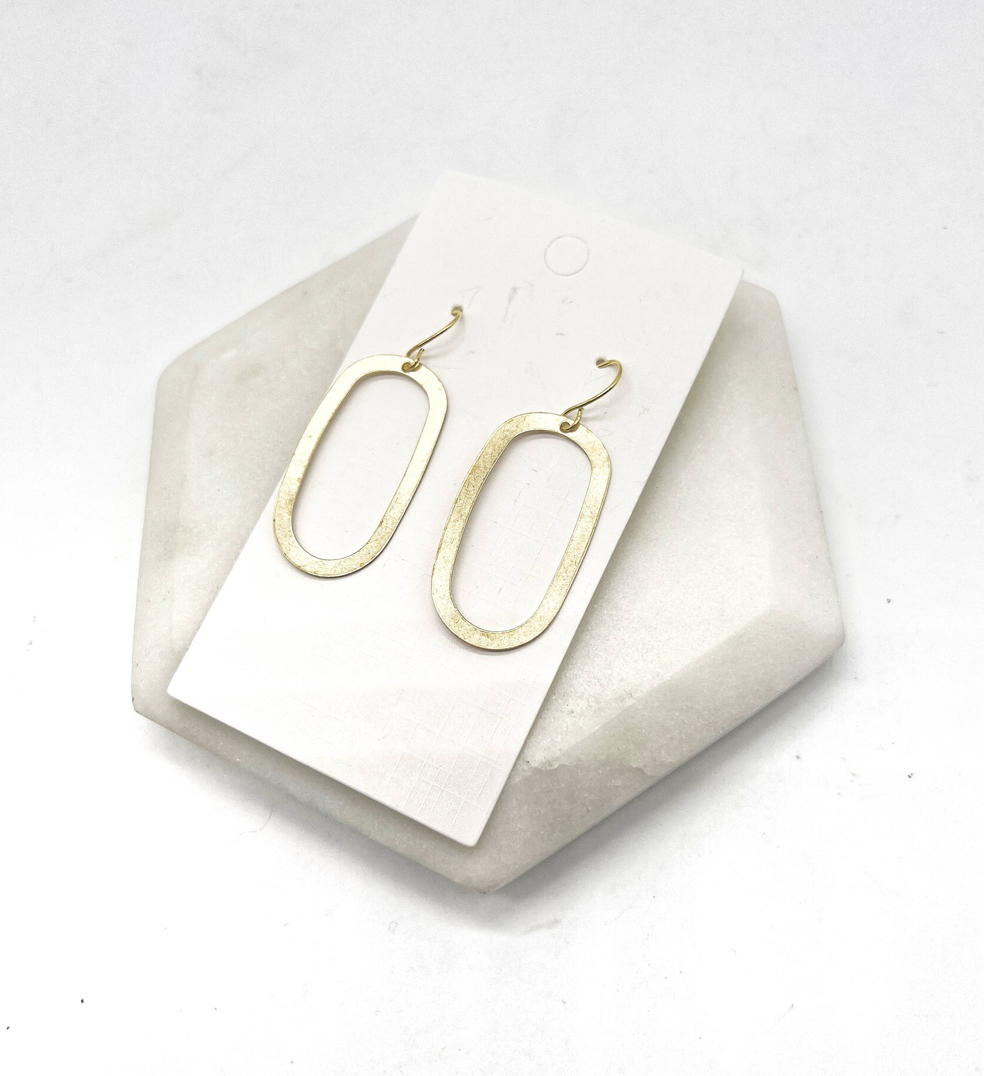 Gold oval earrings on a white card with a geometric stone base