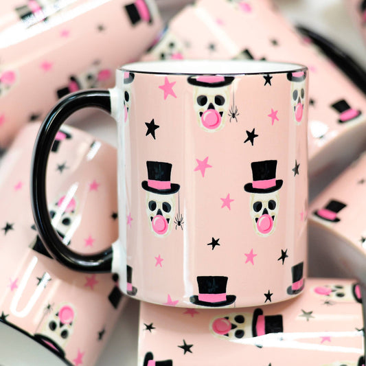 Pink mug with skull and top hat design on a matching pink background