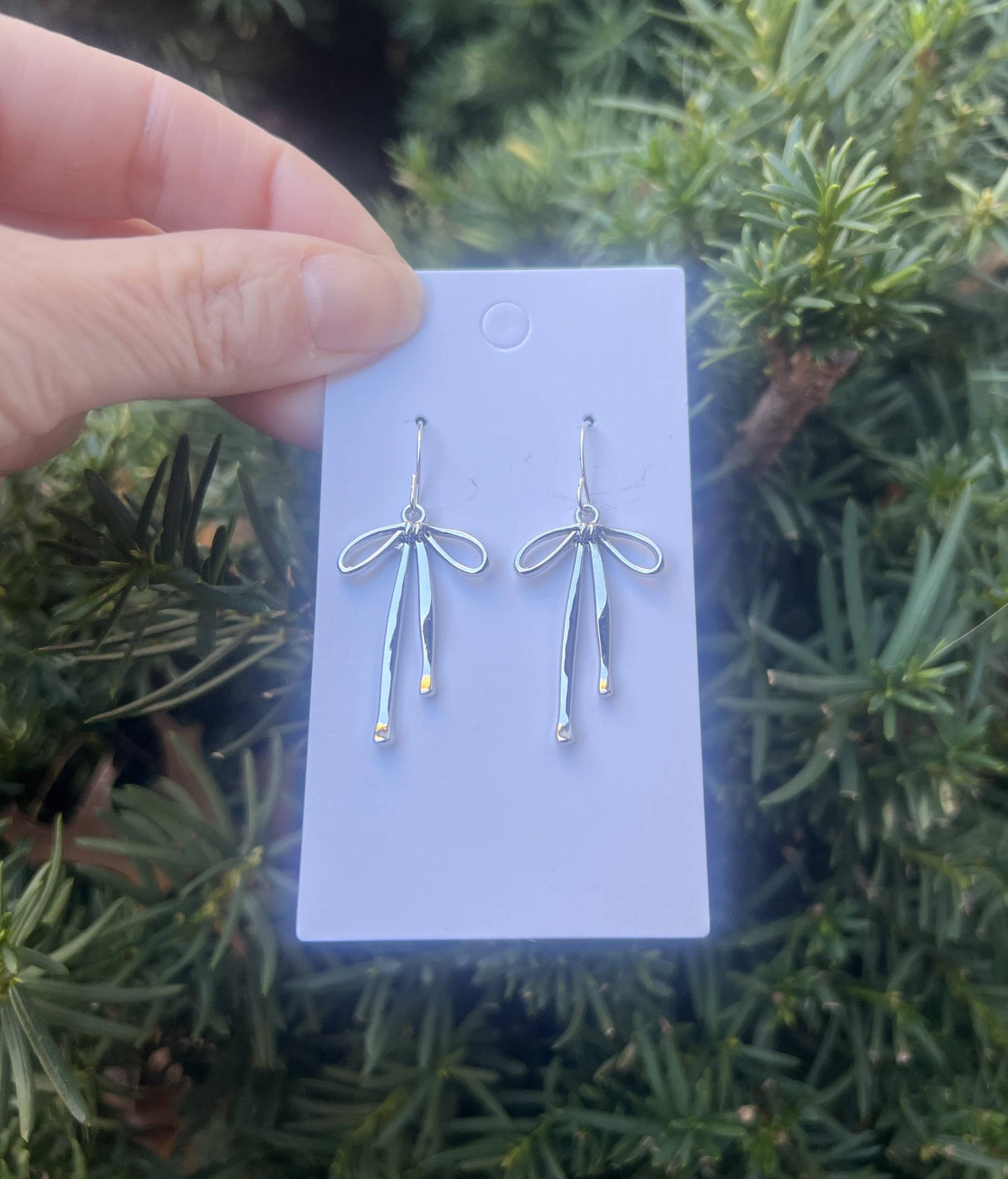 Pair of silver earrings on a white card held against a green leafy background