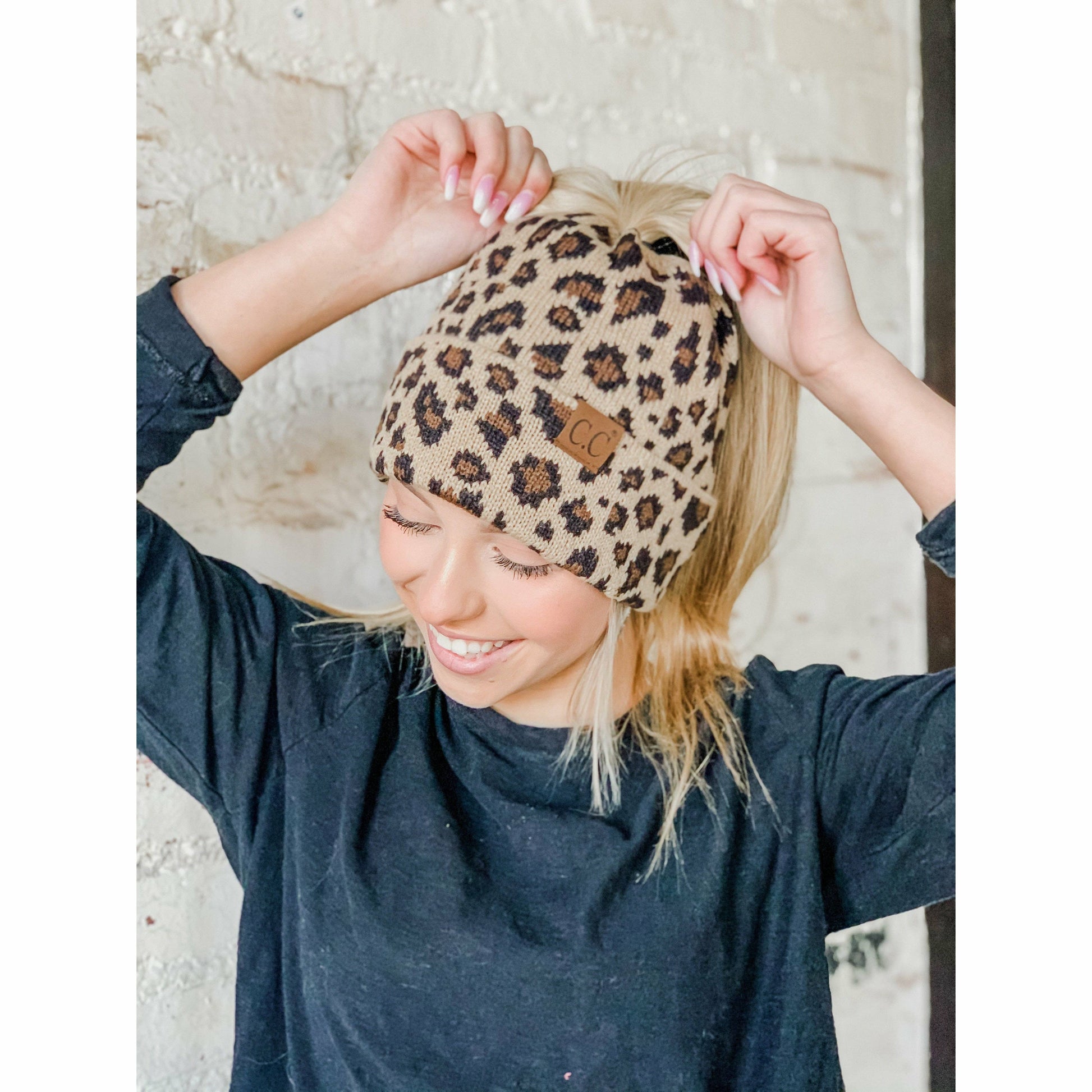 Person wearing a leopard print beanie with a brand logo, smiling against a neutral background